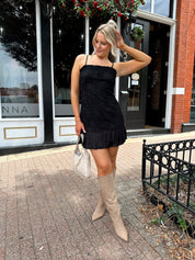 Woman wearing black floral textured mini dress with ruffle hem detail. 