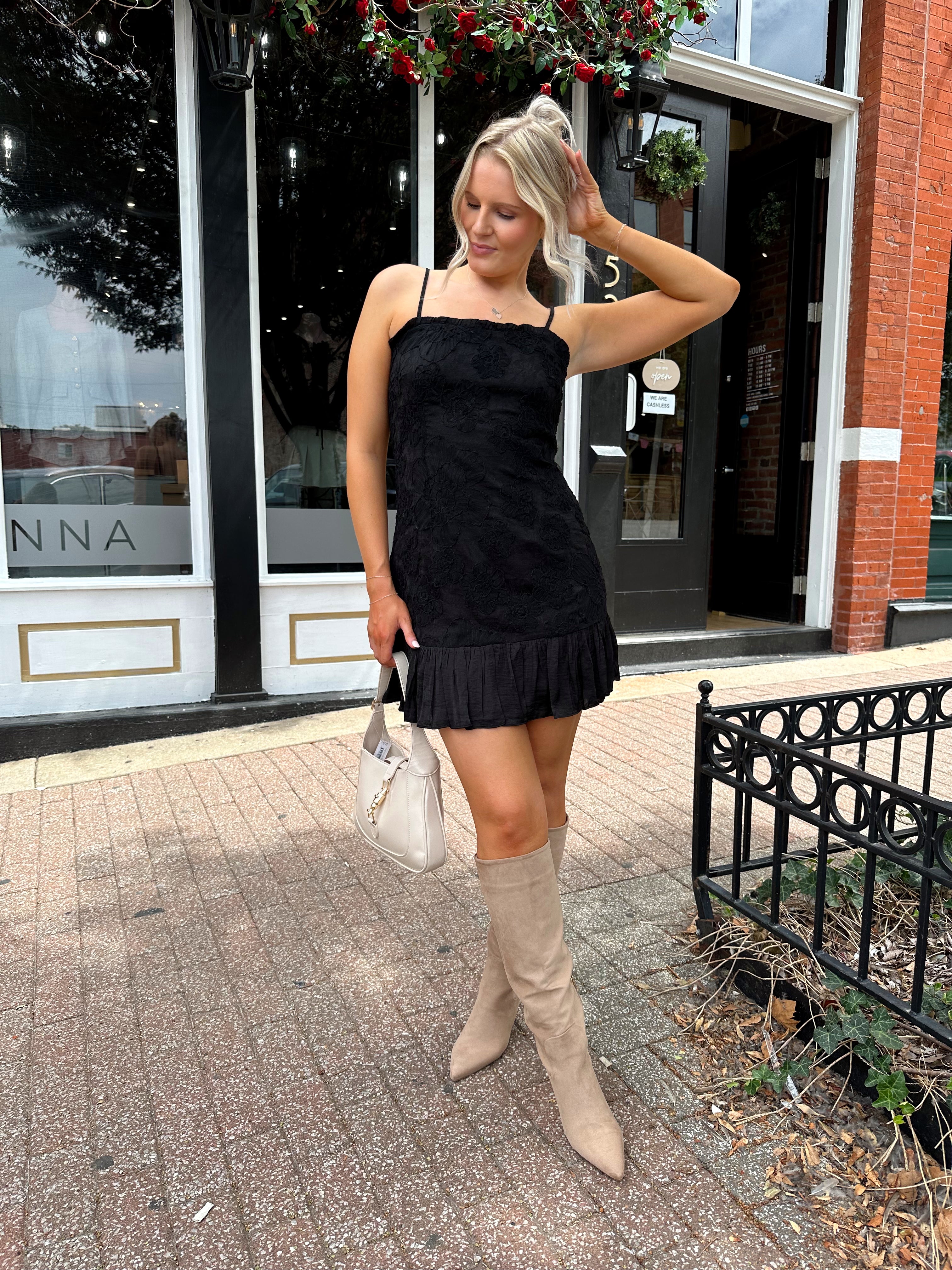 Woman wearing black floral textured mini dress with ruffle hem detail. 