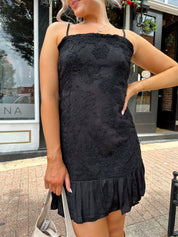 Woman wearing black floral textured mini dress with ruffle hem detail. 