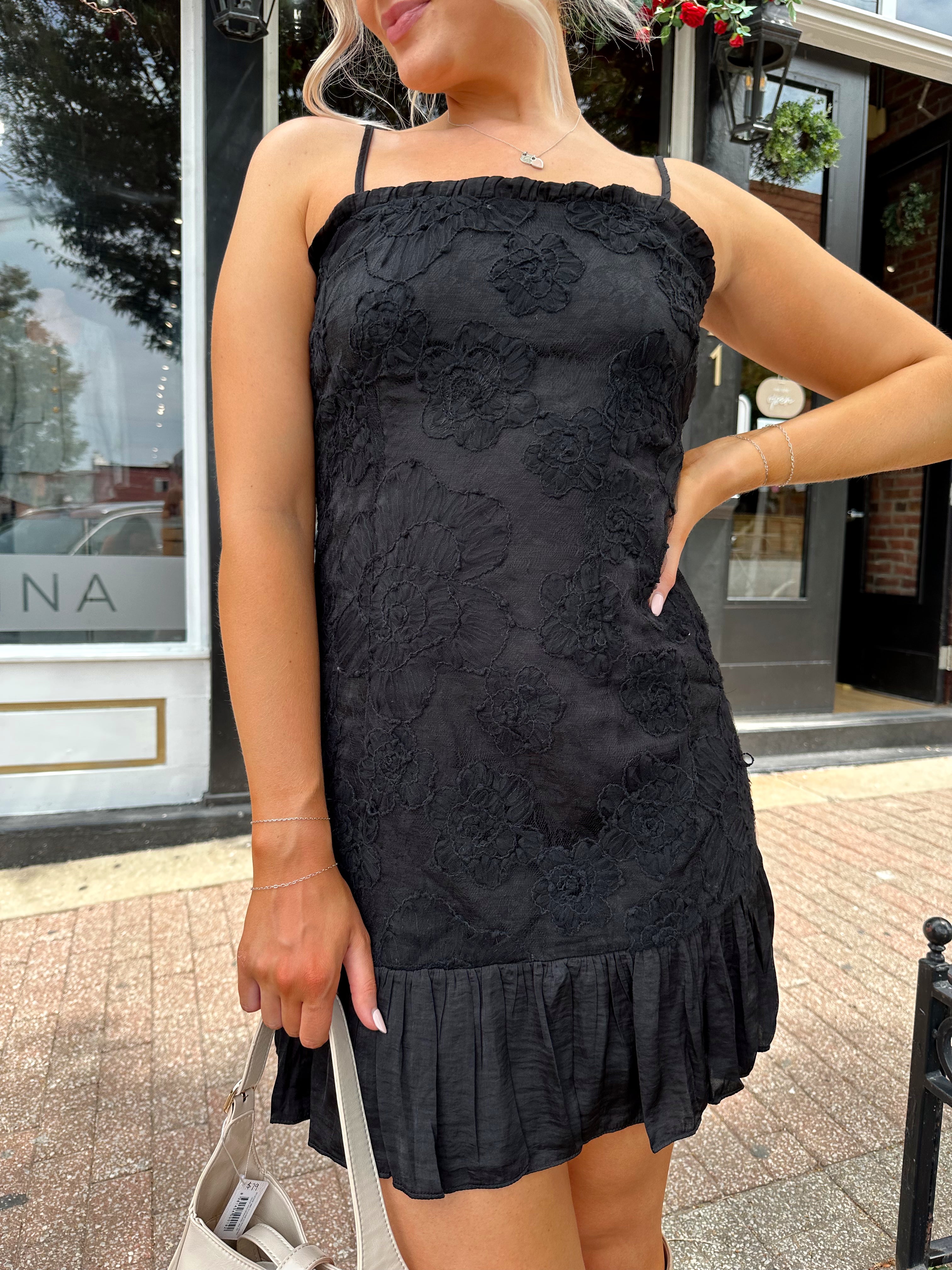 Woman wearing black floral textured mini dress with ruffle hem detail. 