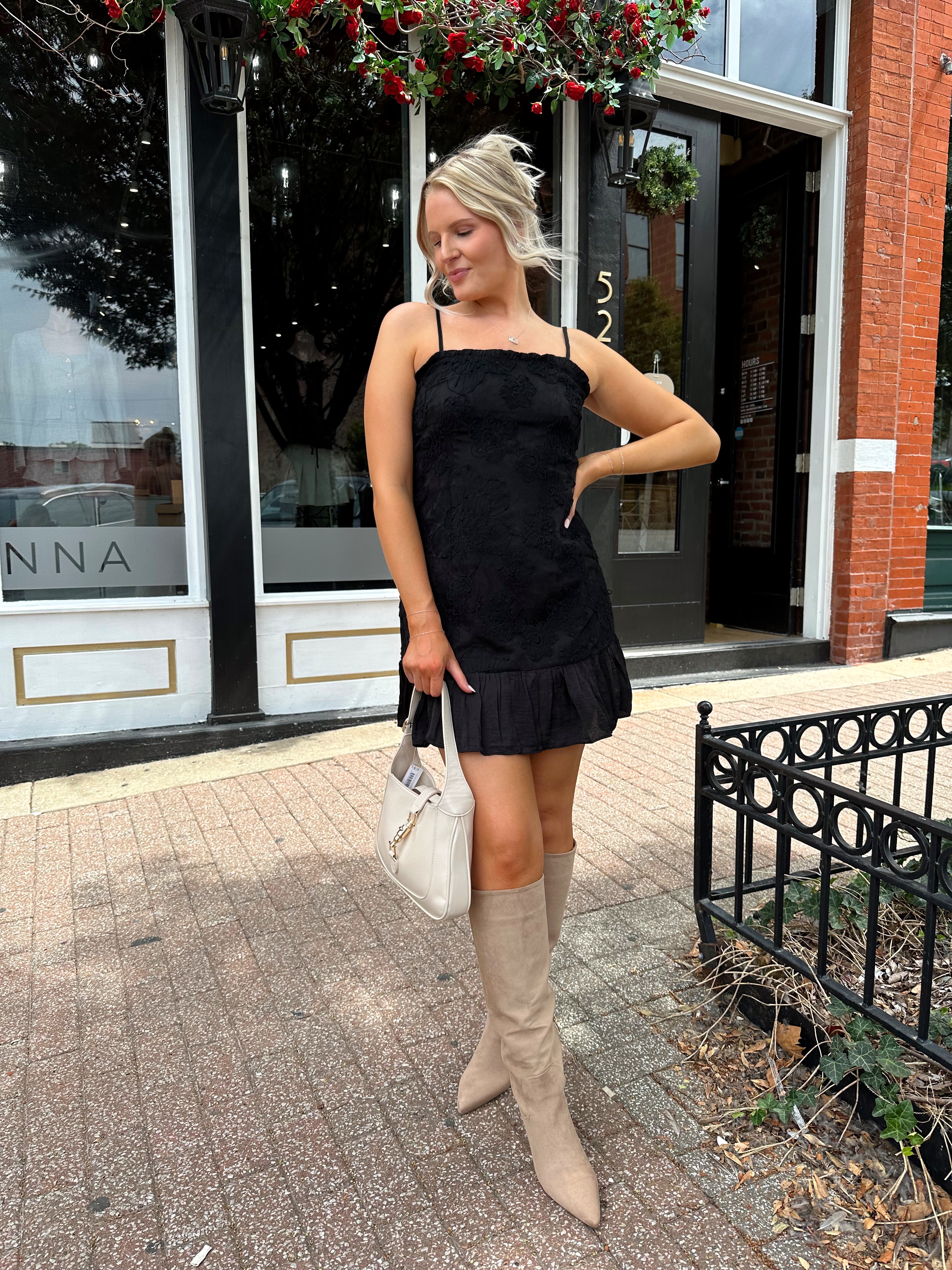 Woman wearing black floral textured mini dress with ruffle hem detail. 