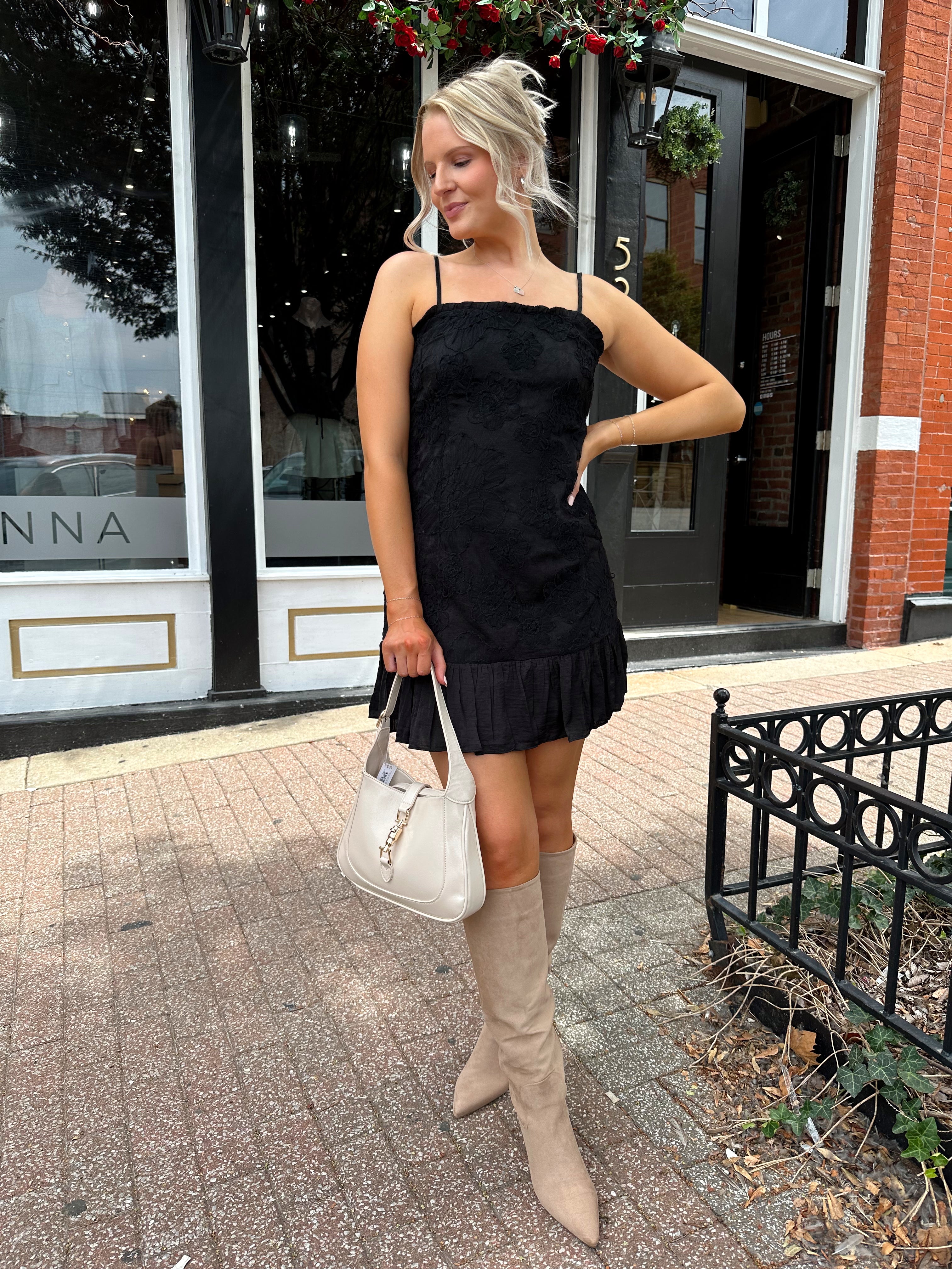Woman wearing black floral textured mini dress with ruffle hem detail. 