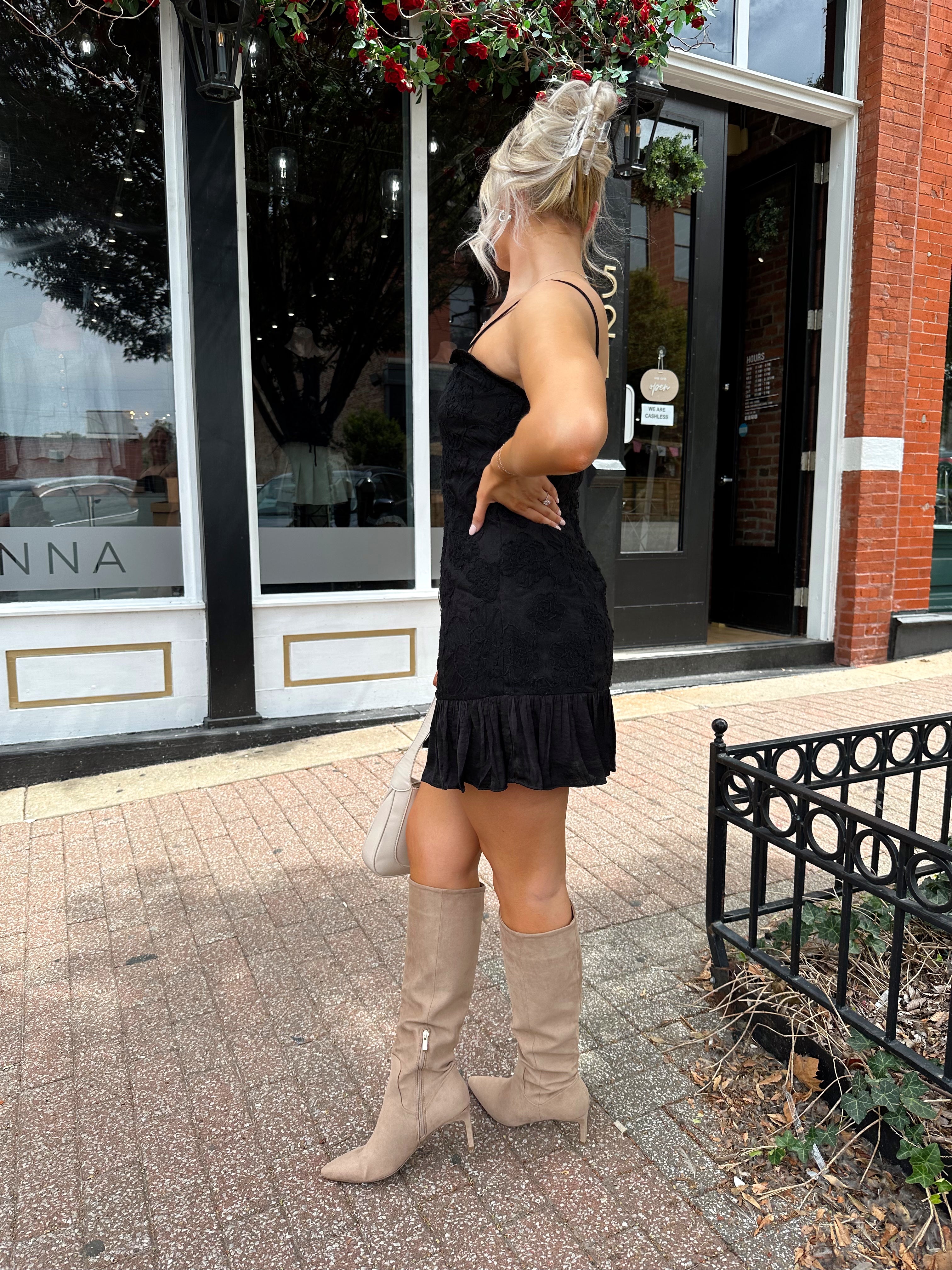 Woman wearing black floral textured mini dress with ruffle hem detail. 
