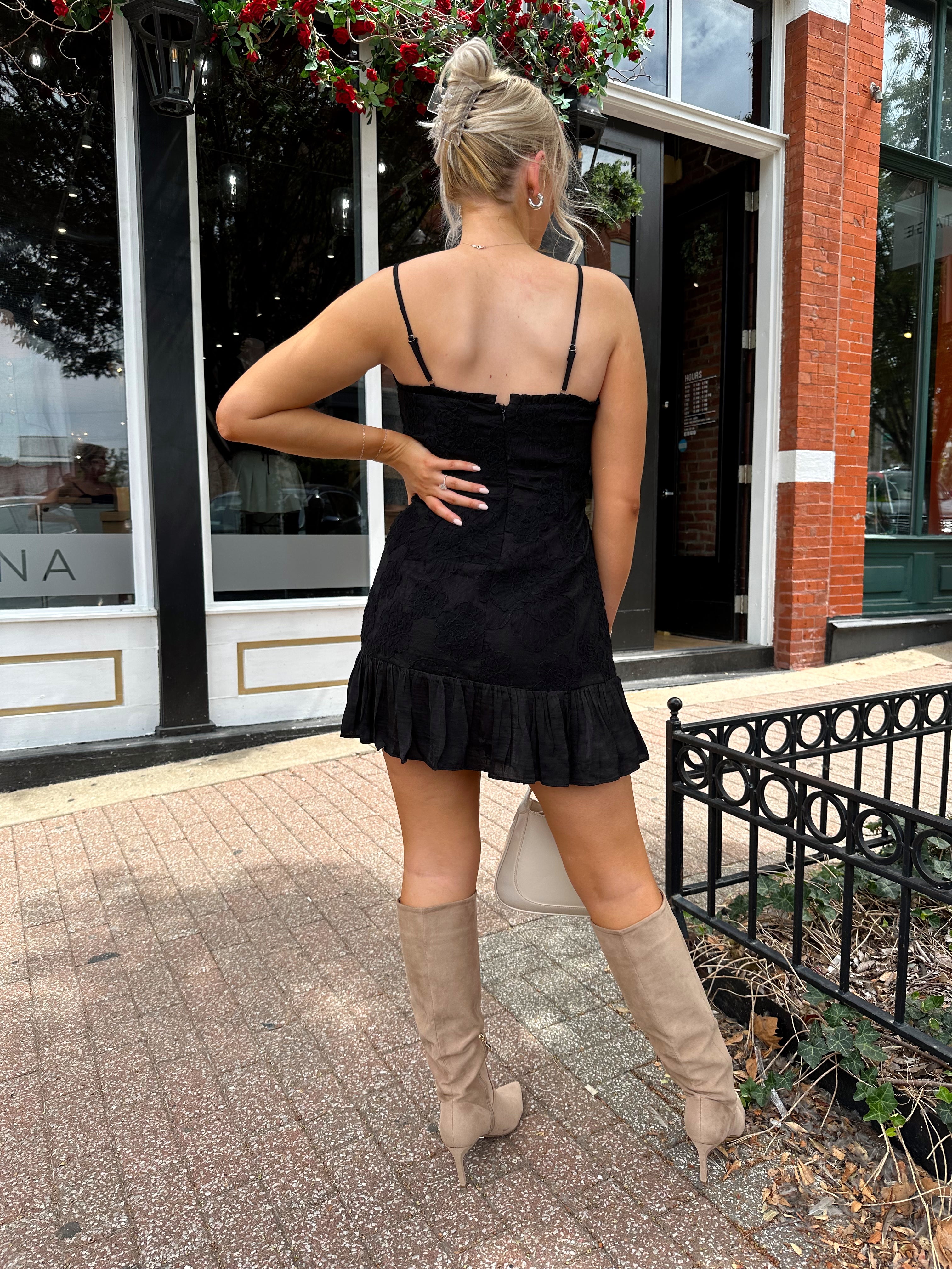 Woman wearing black floral textured mini dress with ruffle hem detail. 