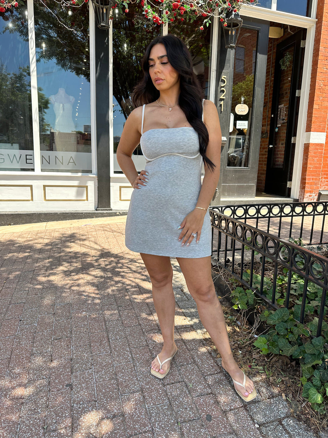 Woman wearing light grey athletic dress, white trim and adjustable spaghetti straps, and built in shorts. 