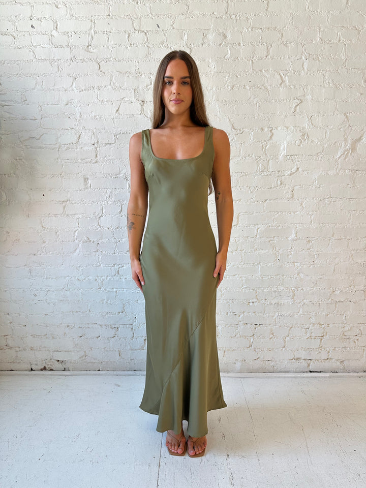 Woman wearing olive green silk maxi dress with lining detailing and scoop neckline. 
