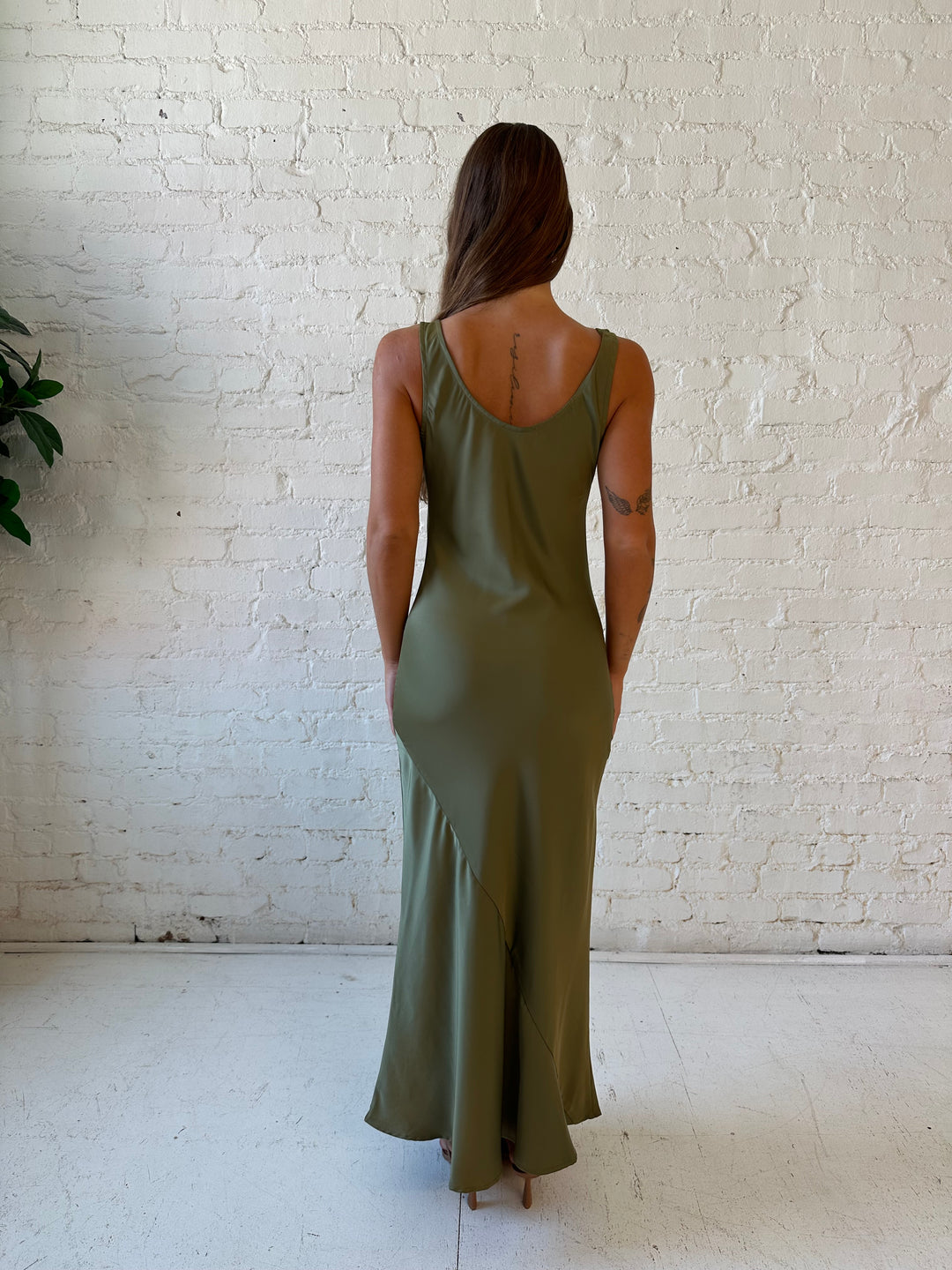 Woman wearing olive green silk maxi dress with lining detailing and scoop neckline. 
