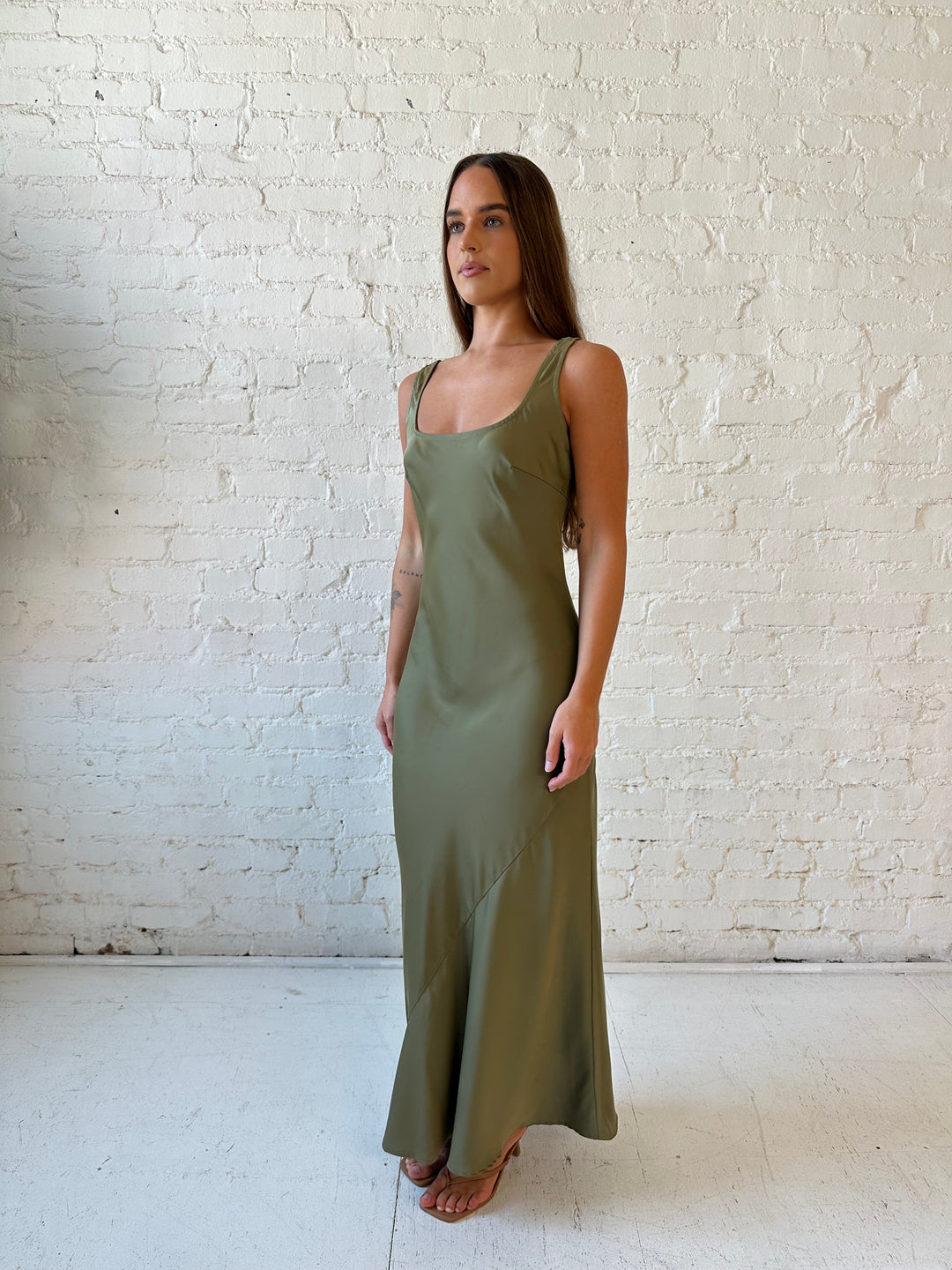 Woman wearing olive green silk maxi dress with lining detailing and scoop neckline. 