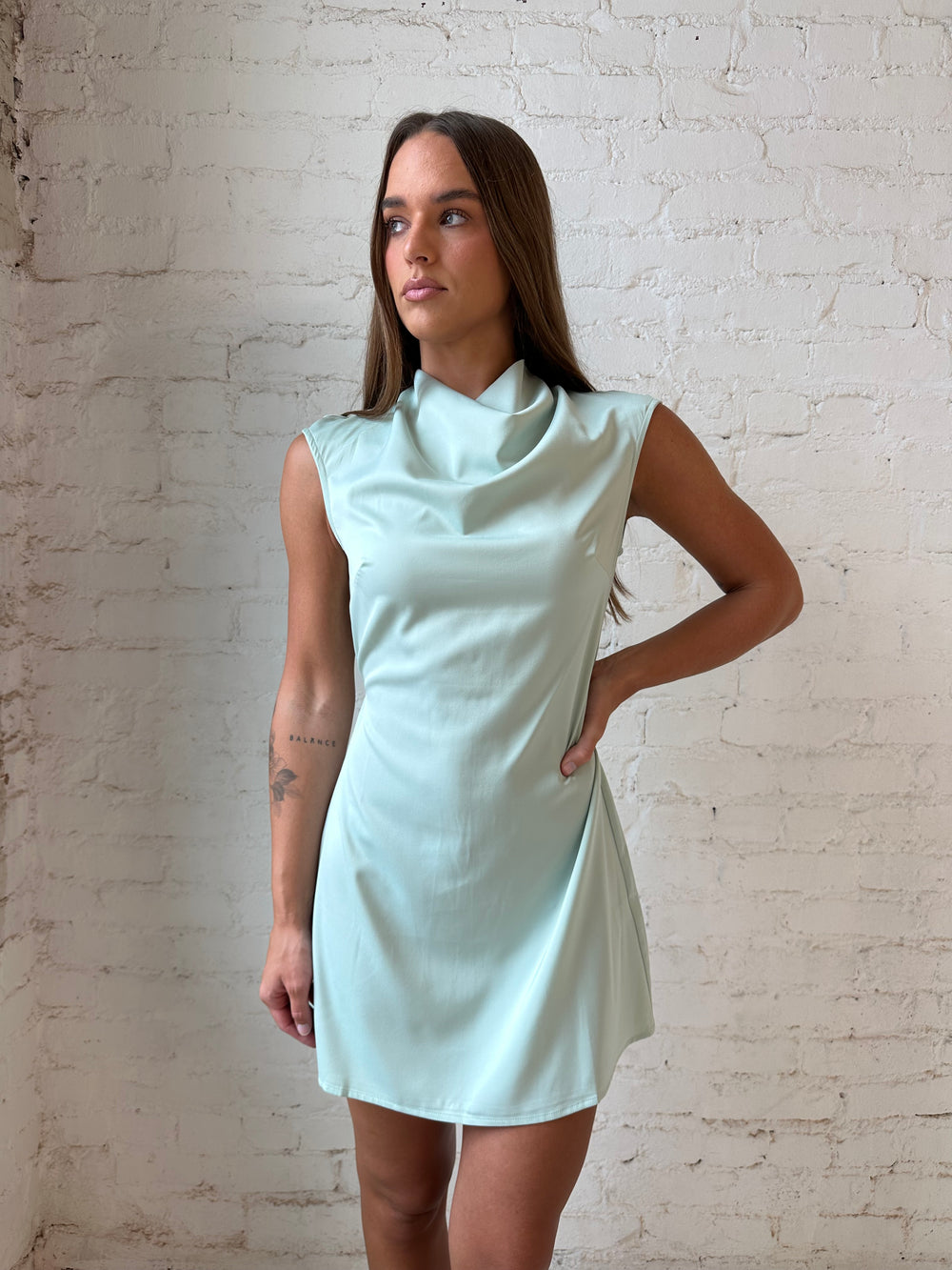 Woman wearing sage green satin mini dress with cap sleeves, and back tie detail.