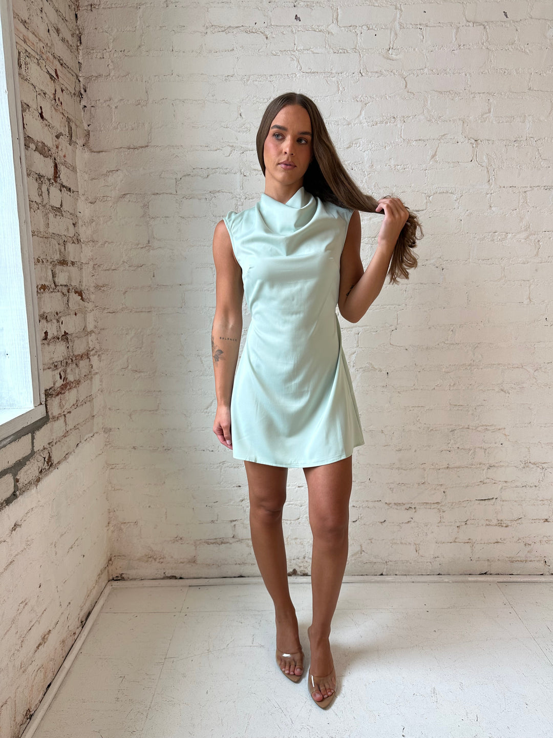 Woman wearing sage green satin mini dress with cap sleeves, and back tie detail.