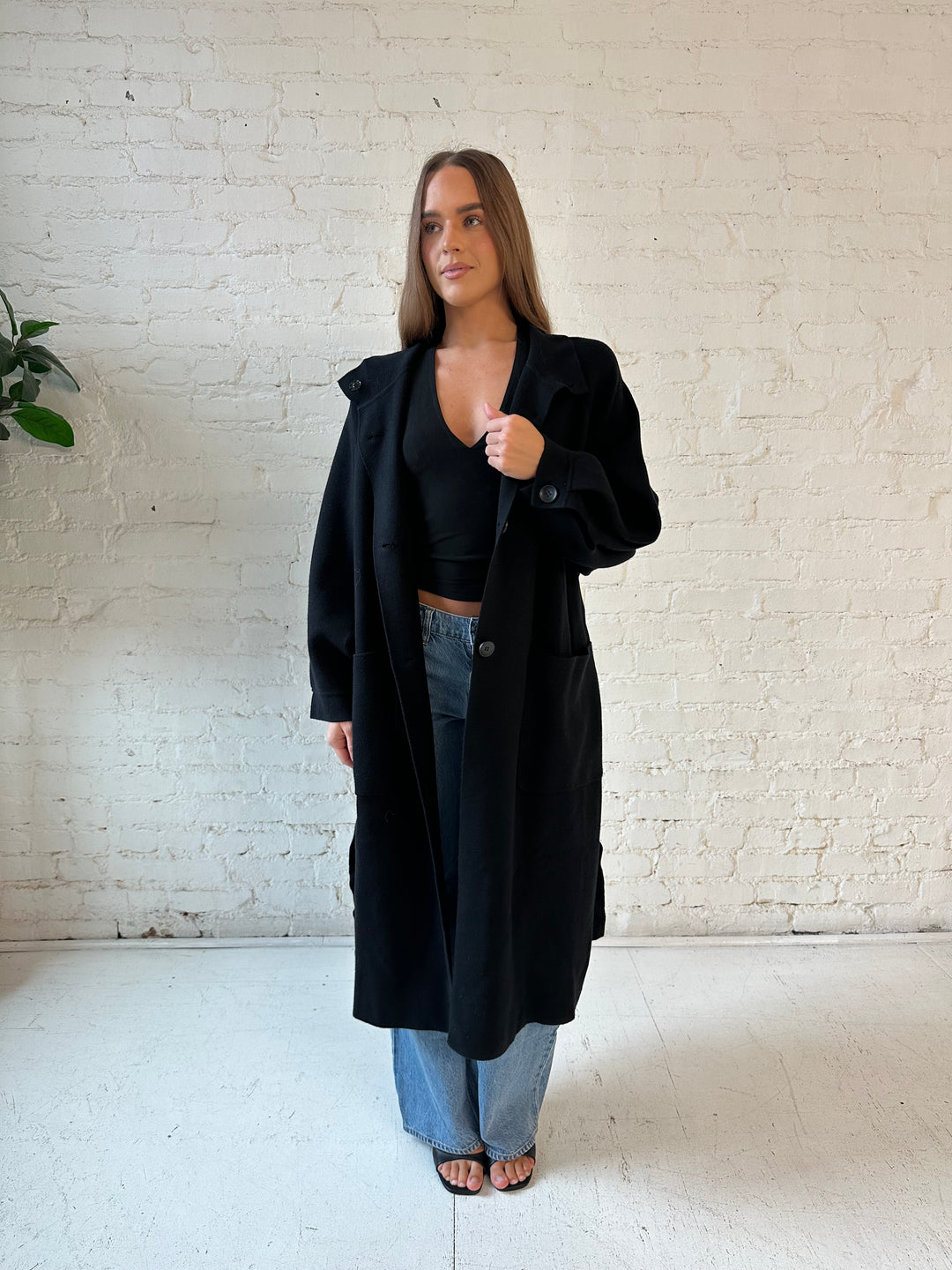 Woman wearing black heavy knit belted duster cardigan with medium wash jean. 