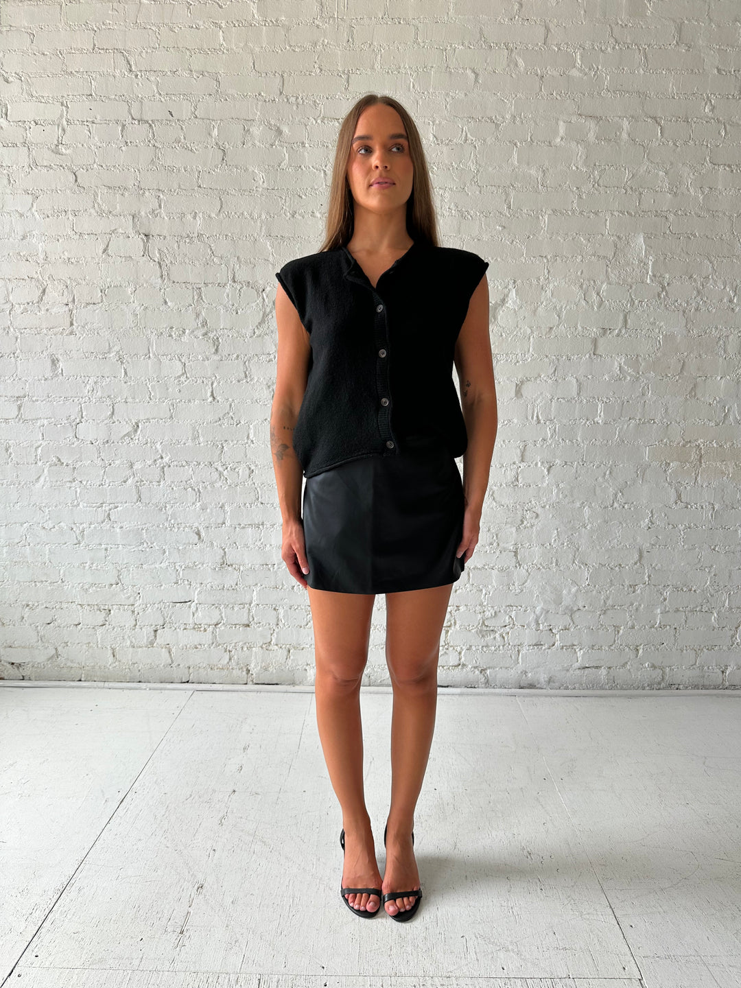 Woman wearing black knit short sleeve button down cardigan with black leather skort. 