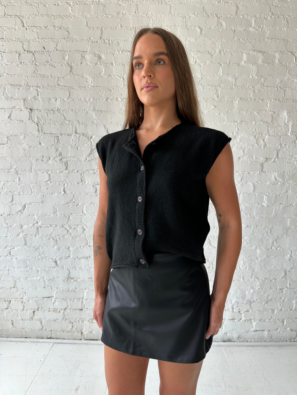 Woman wearing black knit short sleeve button down cardigan with black leather skort. 