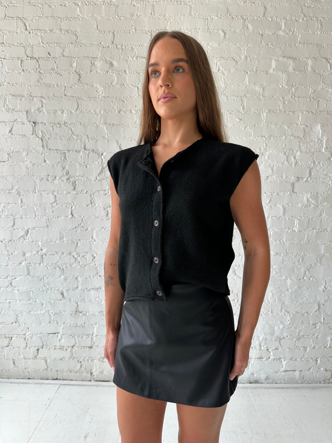 Woman wearing black knit short sleeve button down cardigan with black leather skort. 