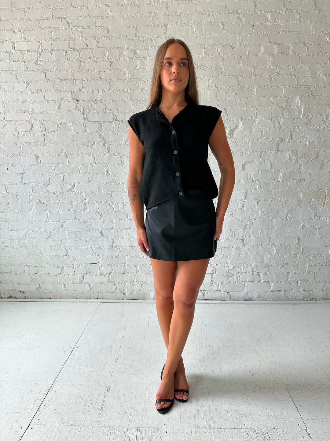 Woman wearing black knit short sleeve button down cardigan with black leather skort. 
