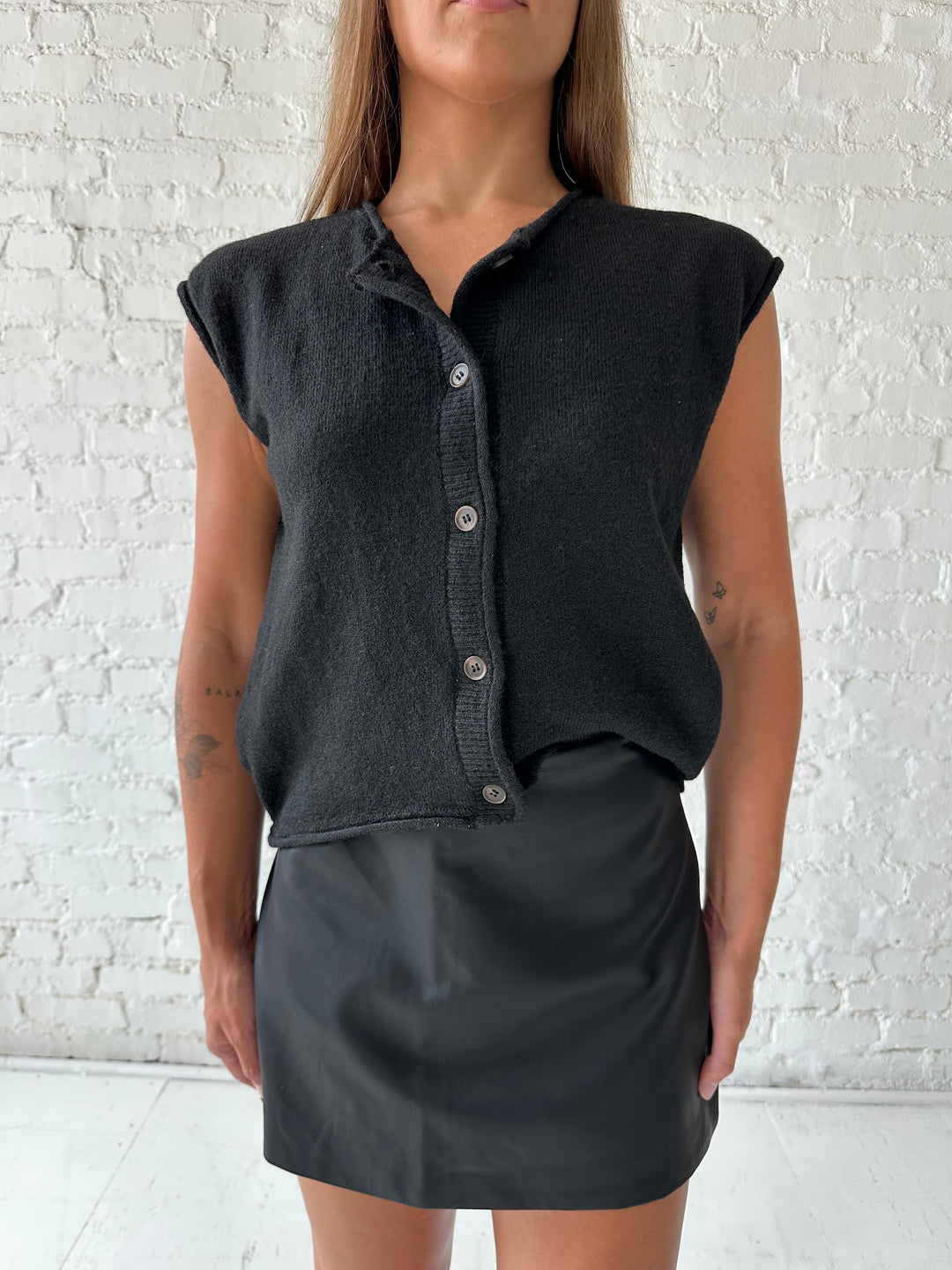 Woman wearing black knit short sleeve button down cardigan with black leather skort. 