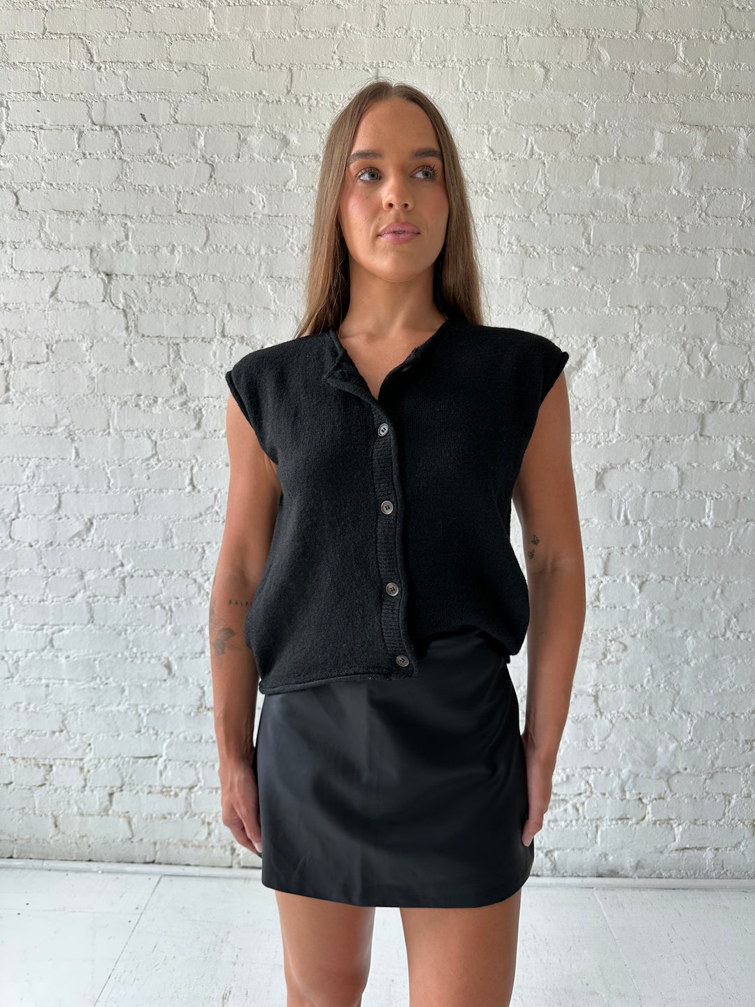 Woman wearing black knit short sleeve button down cardigan with black leather skort. 