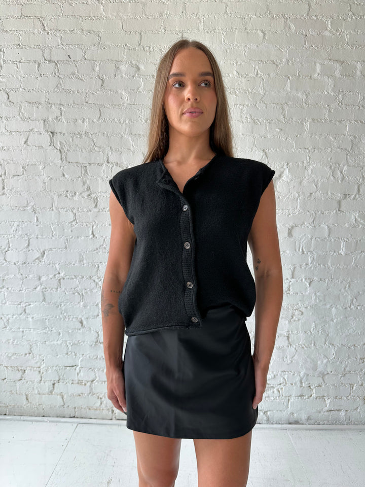 Woman wearing black knit short sleeve button down cardigan with black leather skort. 
