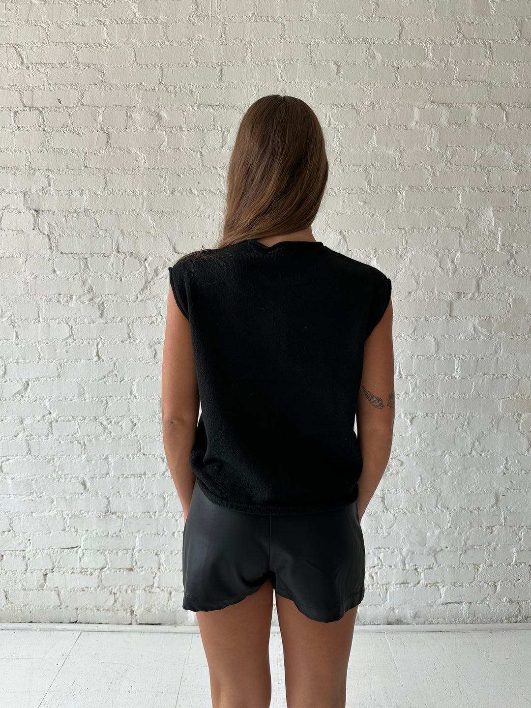 Woman wearing black knit short sleeve button down cardigan with black leather skort. 