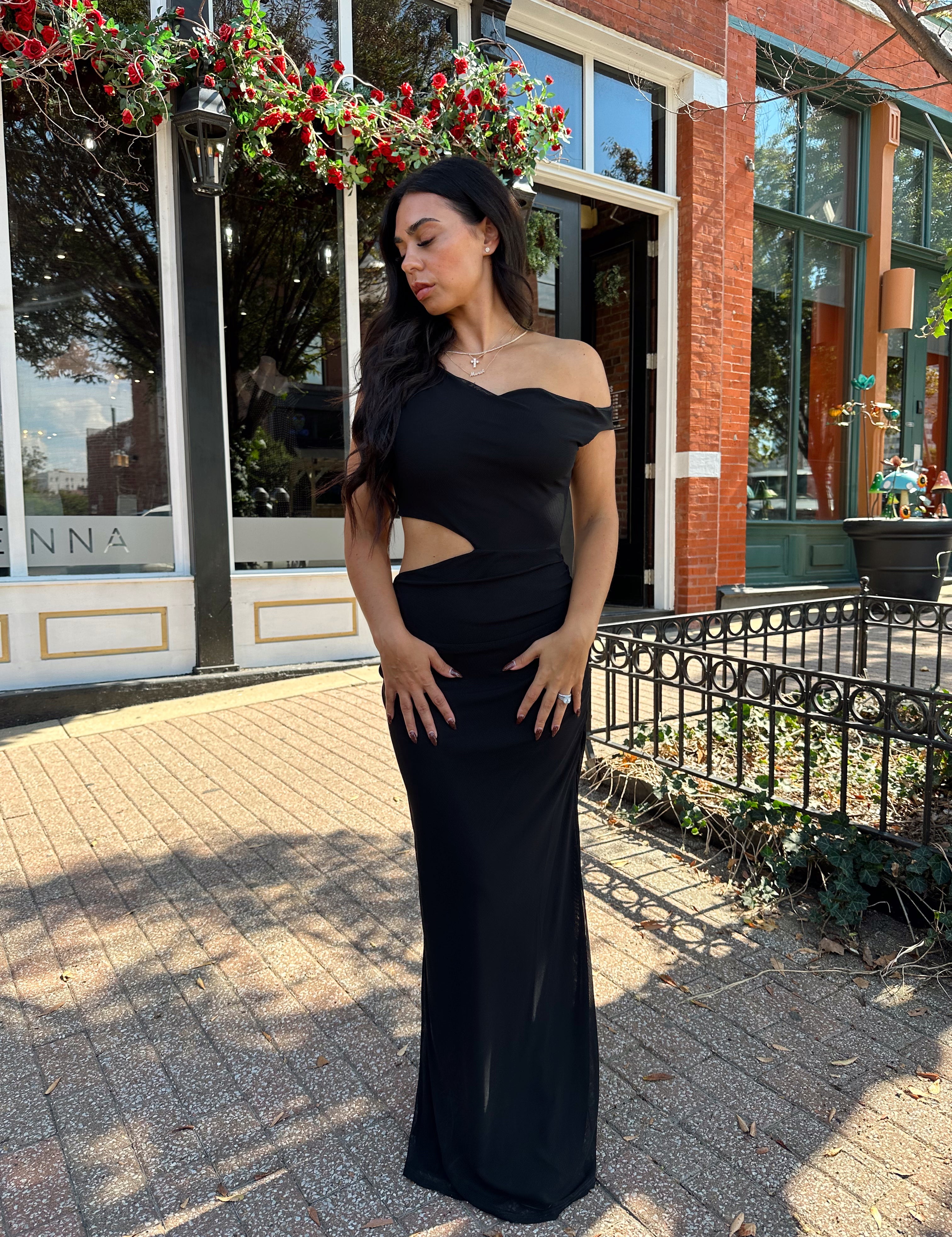 Woman wearing black mesh maxi dress with side cutout, and off the shoulder asymmetrical neckline. 