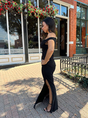 Woman wearing black mesh maxi dress with side cutout, and off the shoulder asymmetrical neckline. 