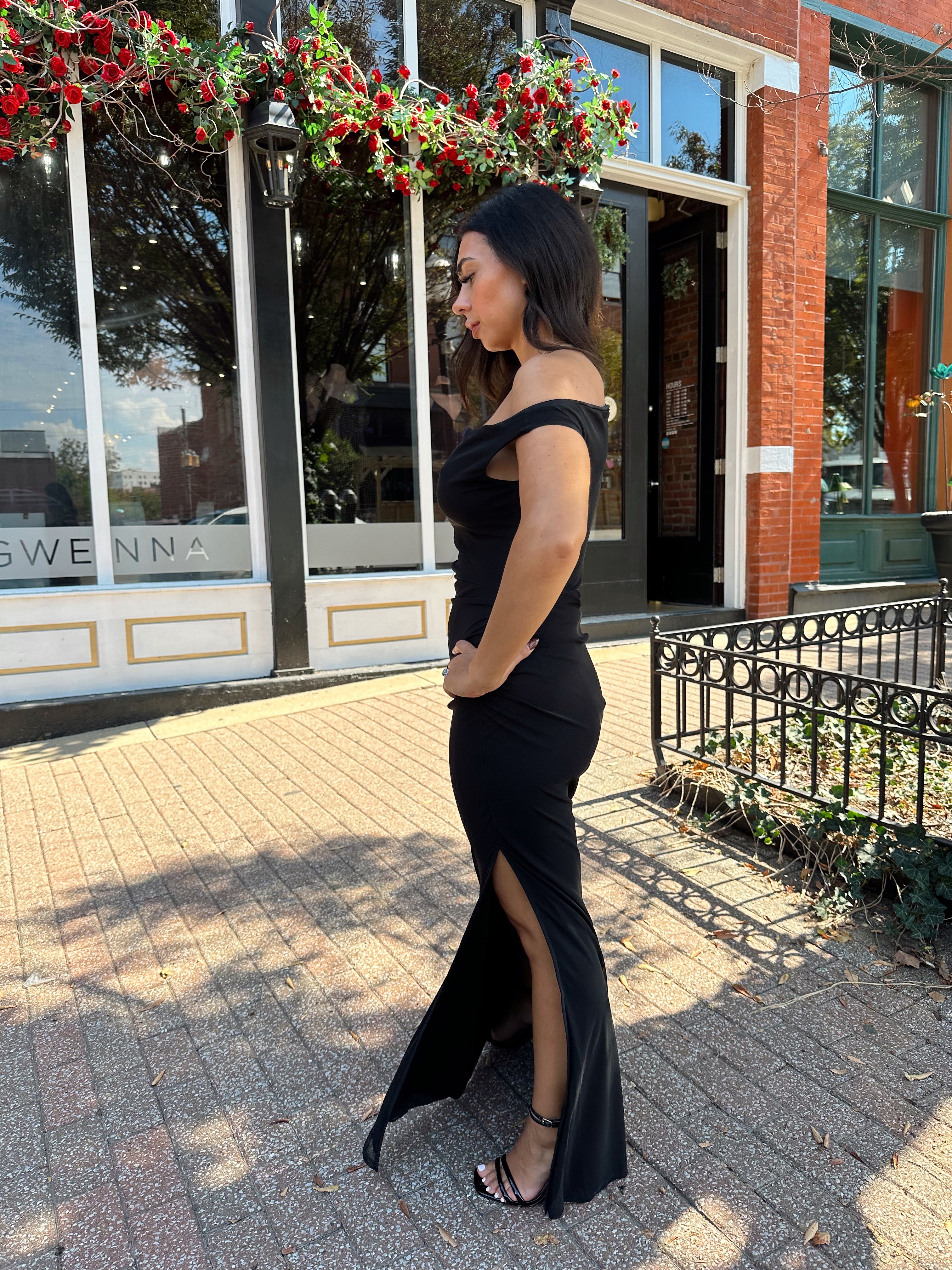 Woman wearing black mesh maxi dress with side cutout, and off the shoulder asymmetrical neckline. 