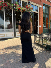 Woman wearing black mesh maxi dress with side cutout, and off the shoulder asymmetrical neckline. 