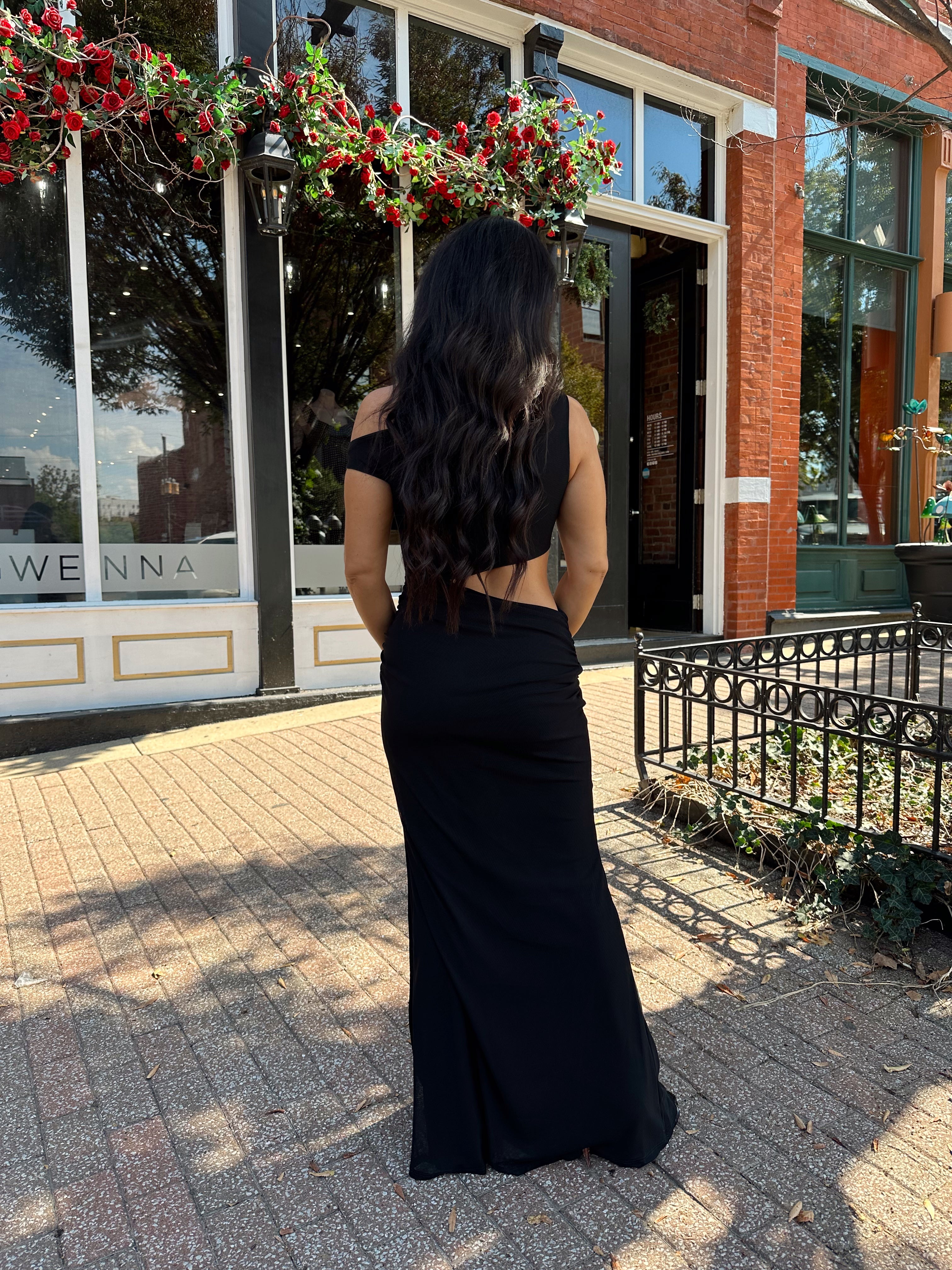 Woman wearing black mesh maxi dress with side cutout, and off the shoulder asymmetrical neckline. 