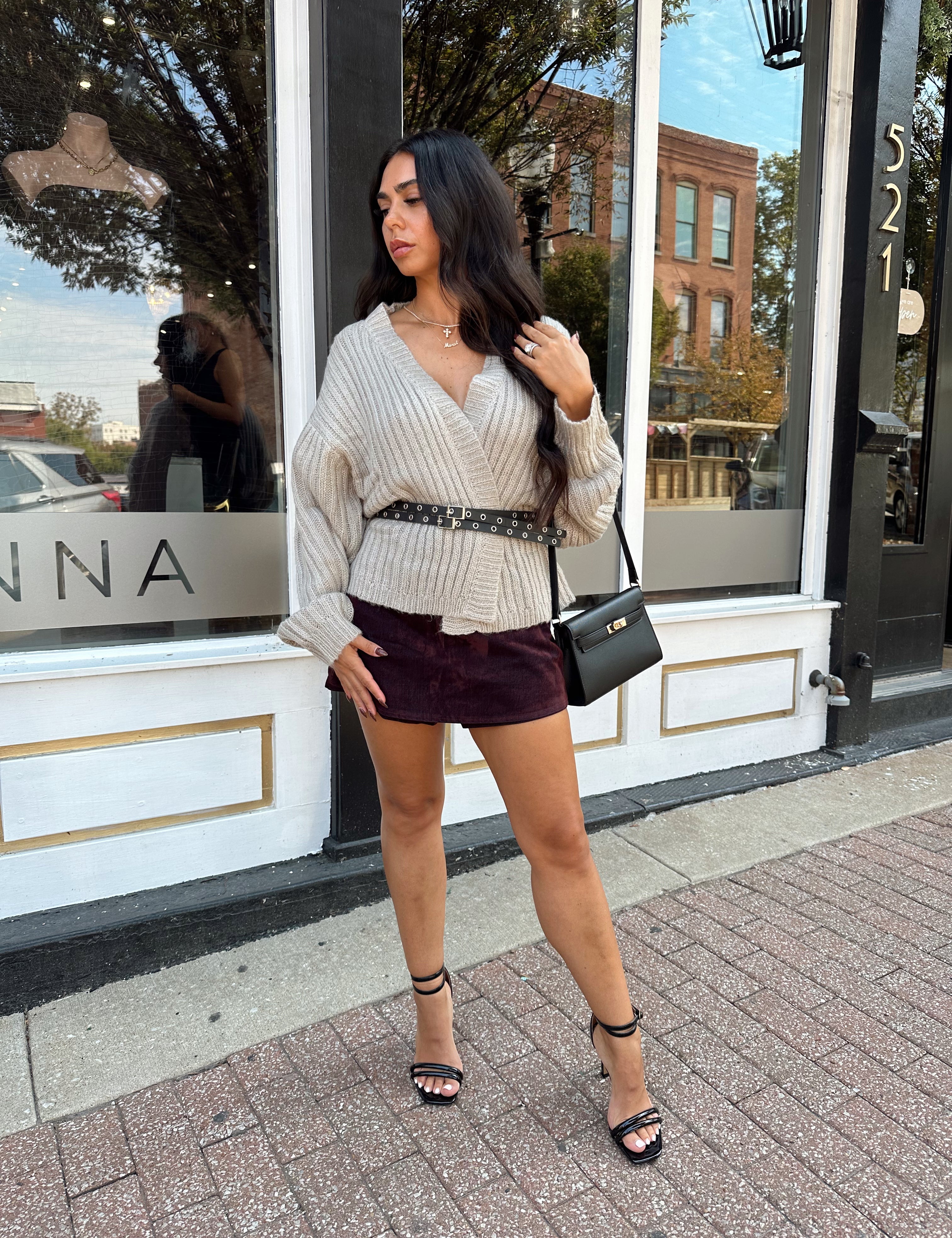 Woman wearing grey knit wrap cardigan with black belted waist. 