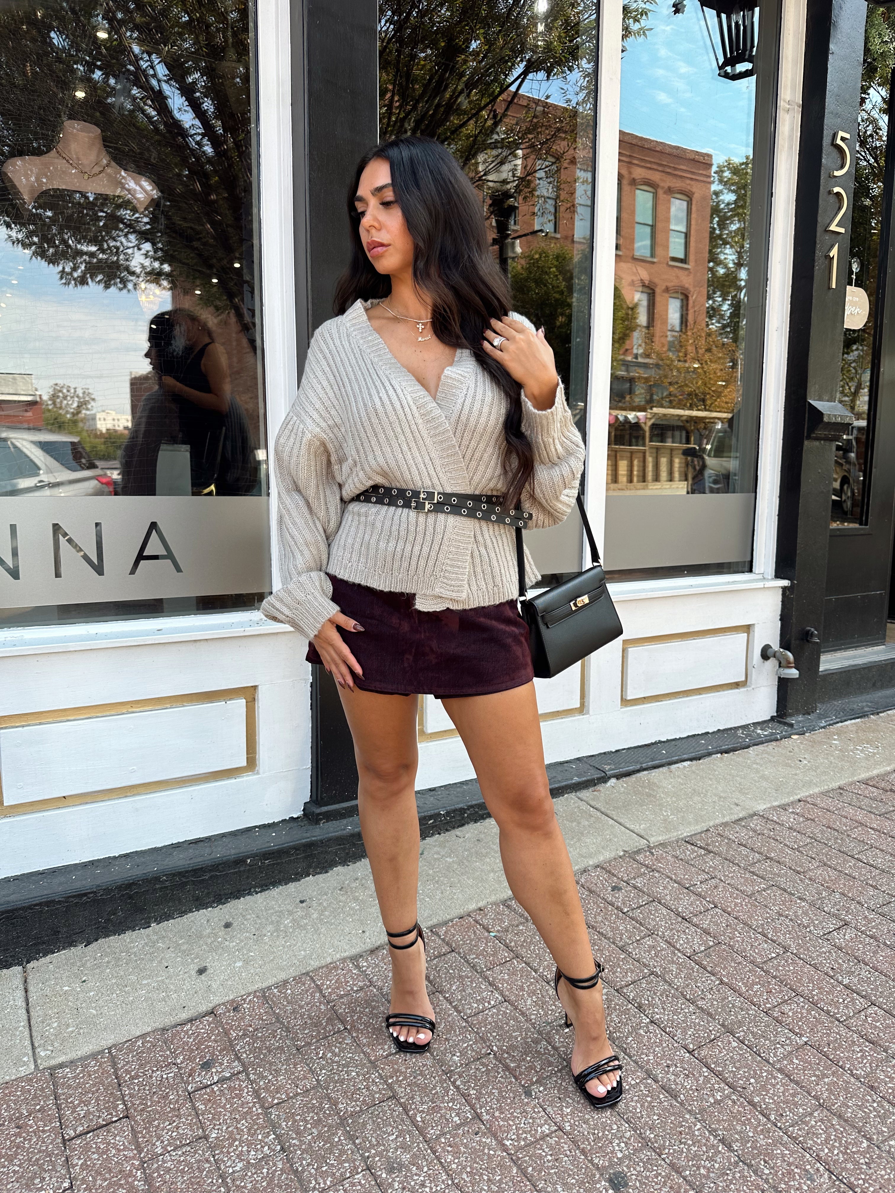 Woman wearing grey knit wrap cardigan with black belted waist. 