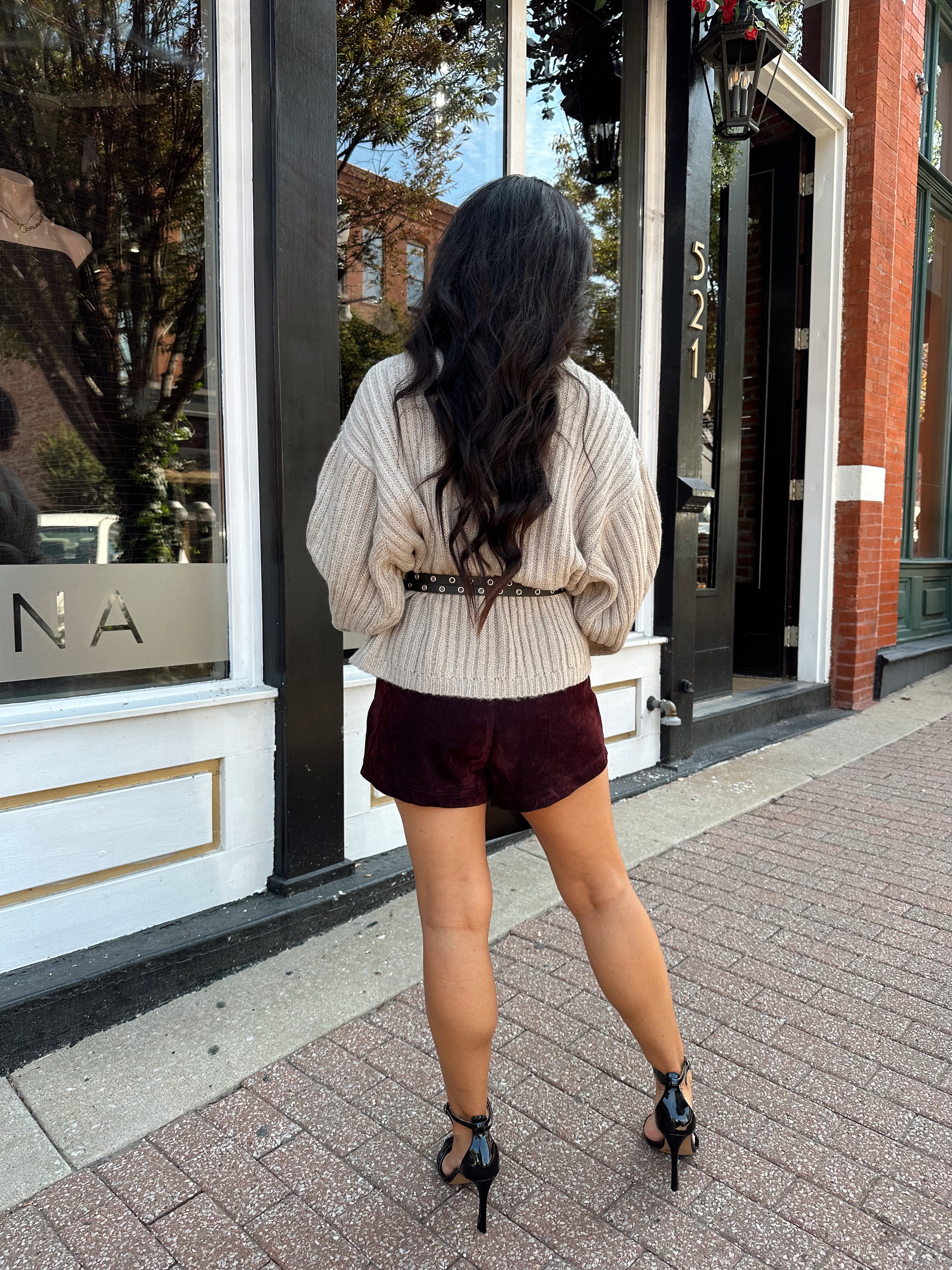 Woman wearing grey knit wrap cardigan with black belted waist. 