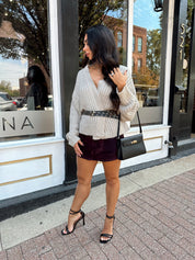 Woman wearing grey knit wrap cardigan with black belted waist. 