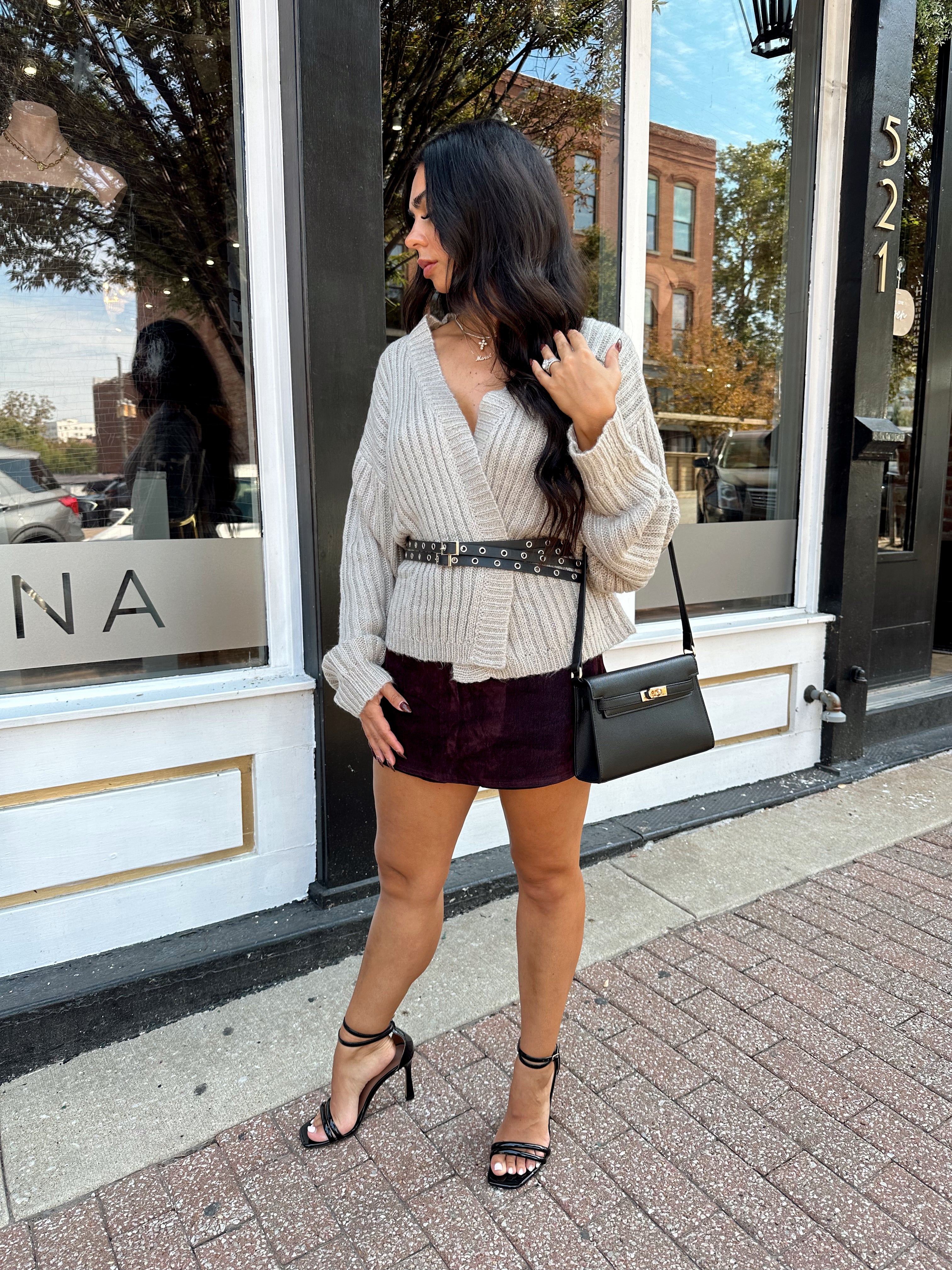Woman wearing grey knit wrap cardigan with black belted waist. 