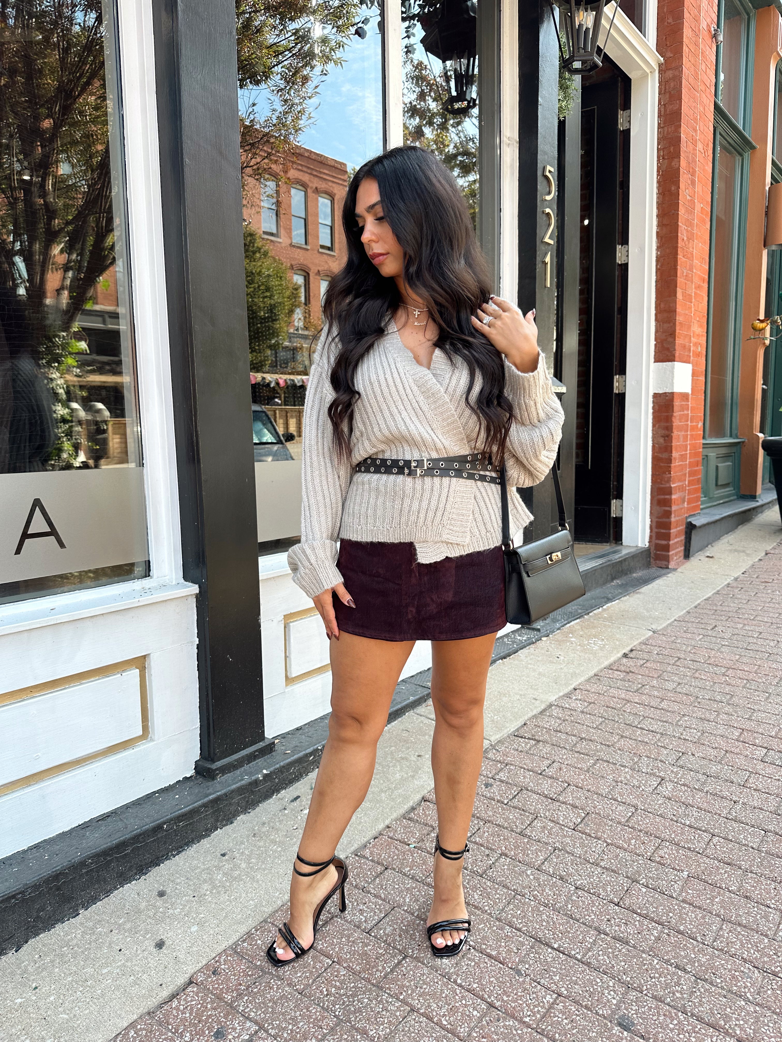 Woman wearing grey knit wrap cardigan with black belted waist. 