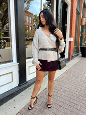 Woman wearing grey knit wrap cardigan with black belted waist. 