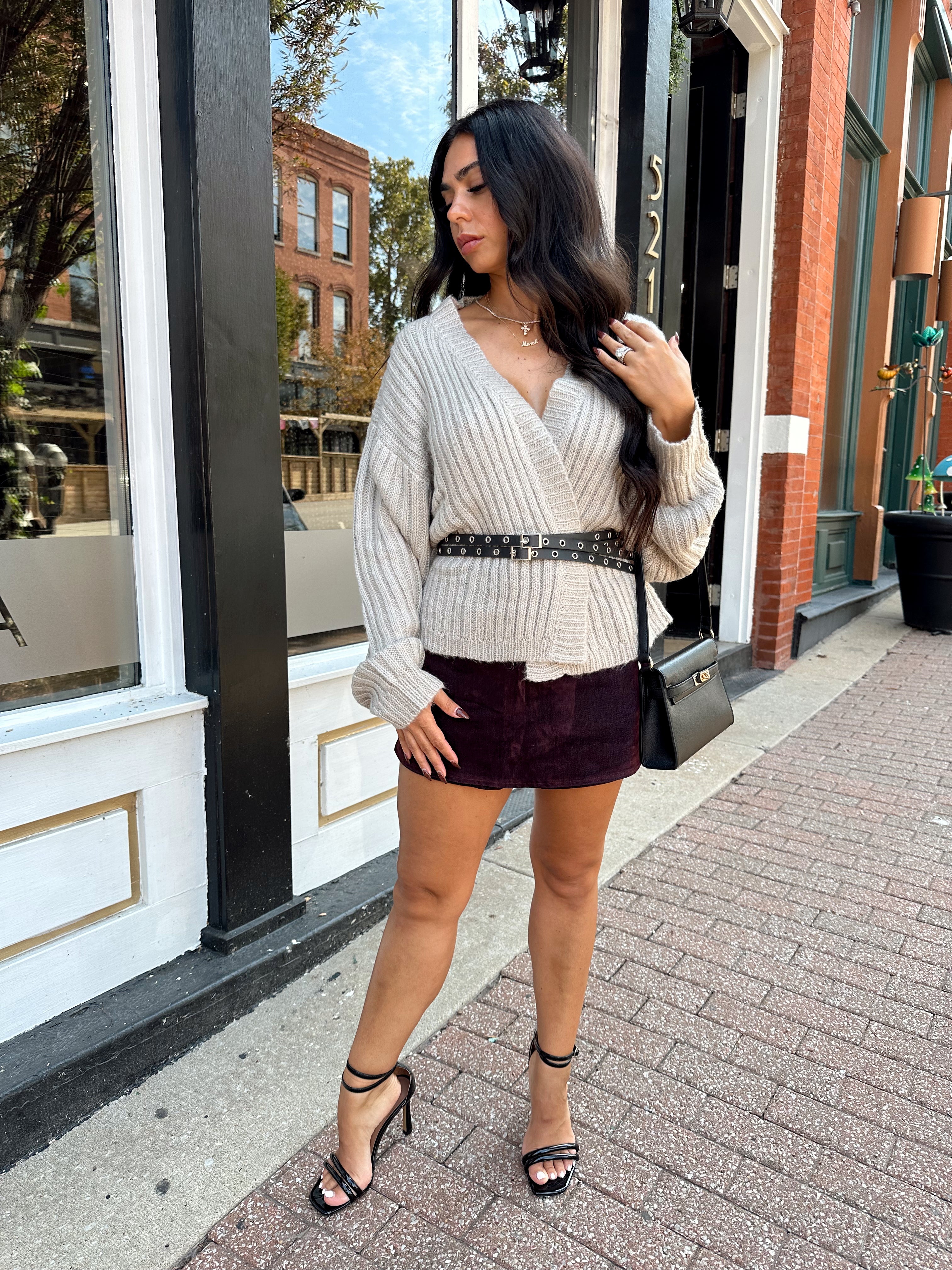 Woman wearing grey knit wrap cardigan with black belted waist. 