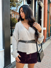 Woman wearing grey knit wrap cardigan with black belted waist. 