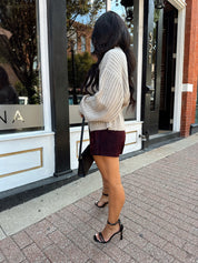 Woman wearing grey knit wrap cardigan with black belted waist. 