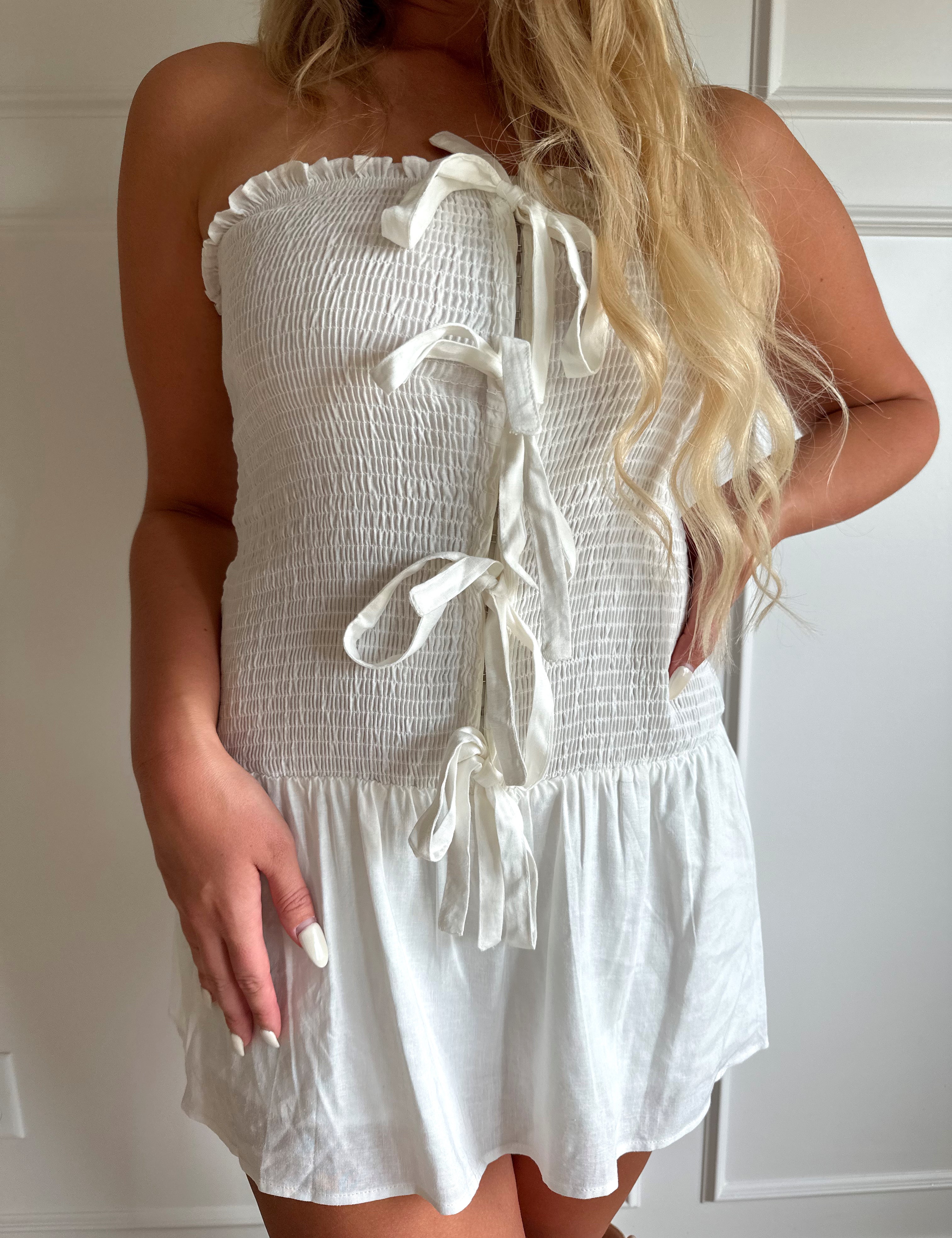 Woman wearing white smocked strapless mini dress with bow detail and clasp closure.