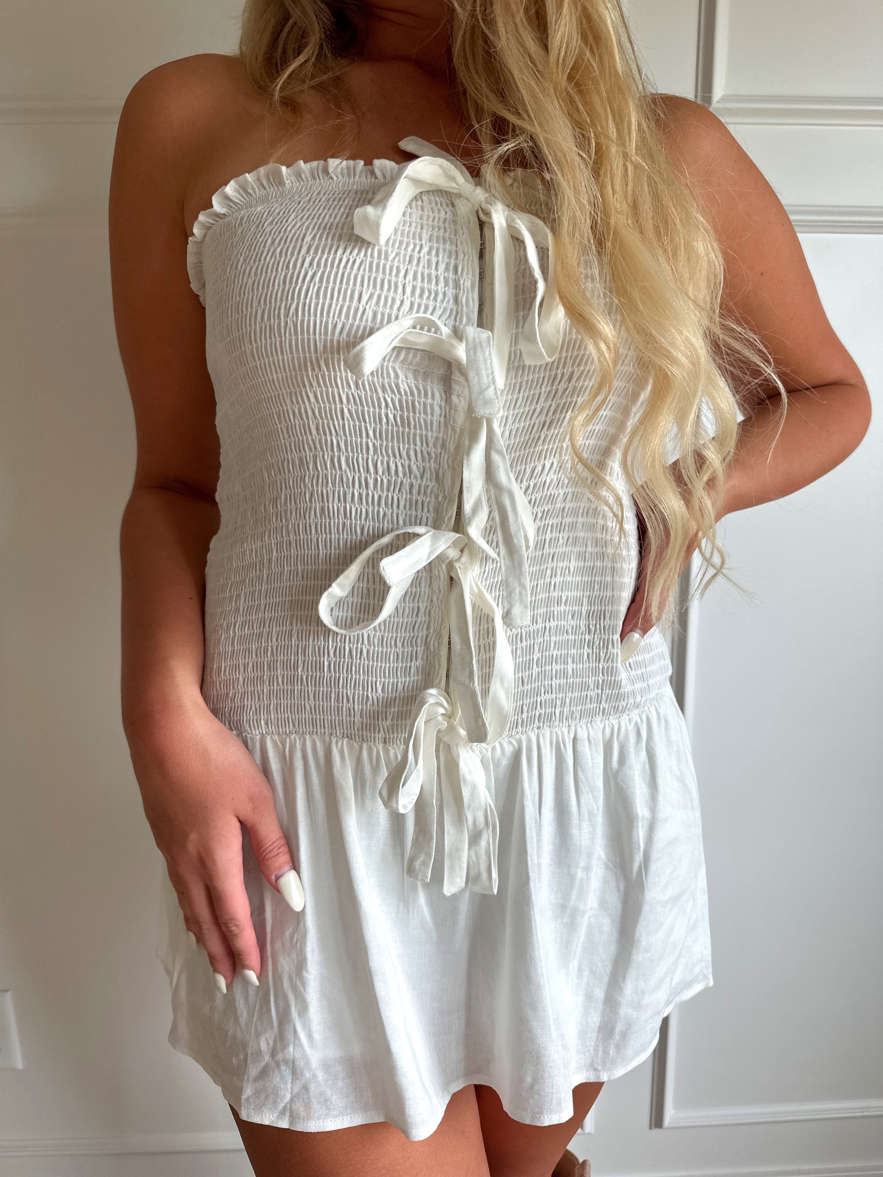 Woman wearing white smocked strapless mini dress with bow detail and clasp closure.