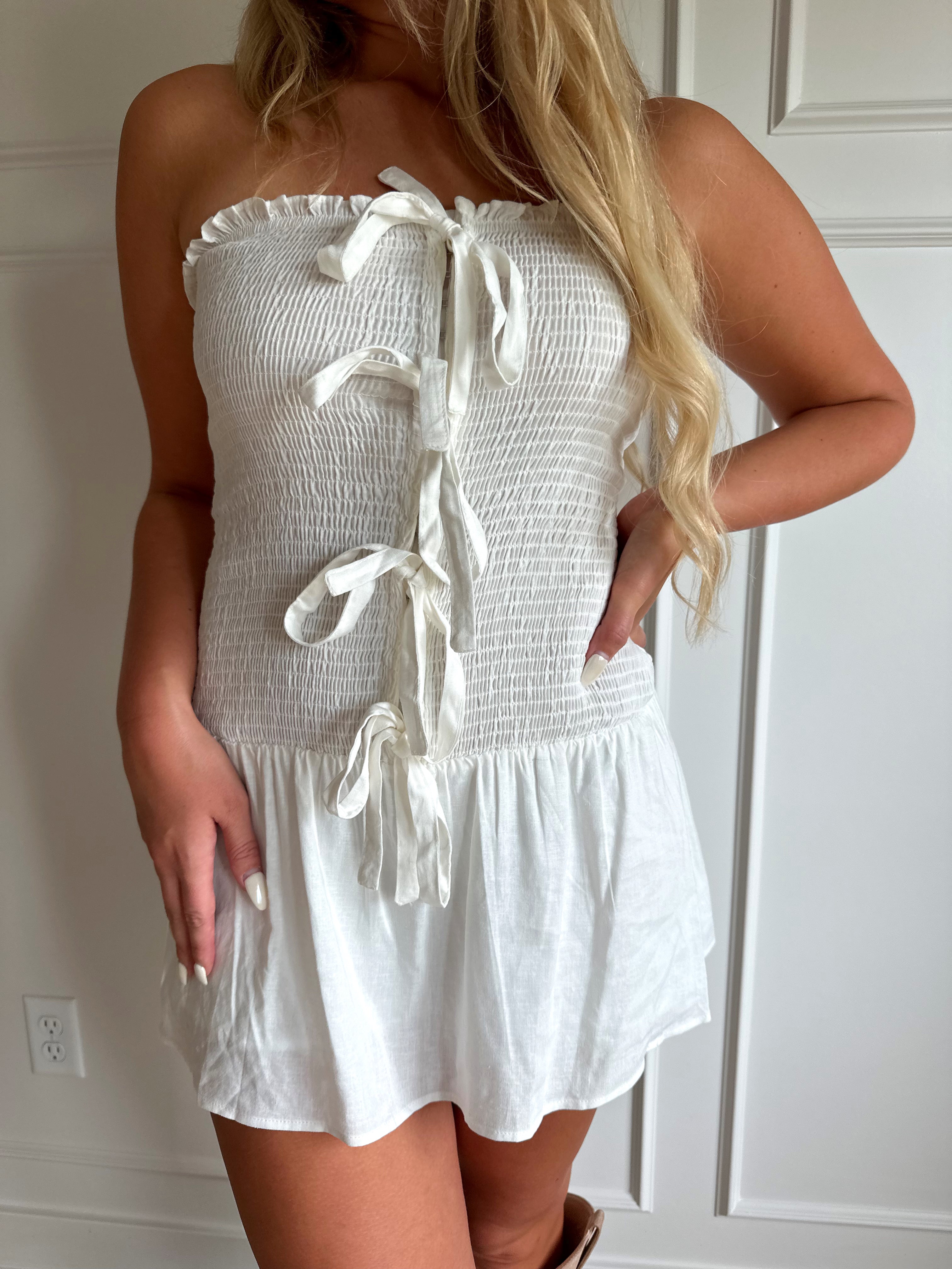 Woman wearing white smocked strapless mini dress with bow detail and clasp closure.
