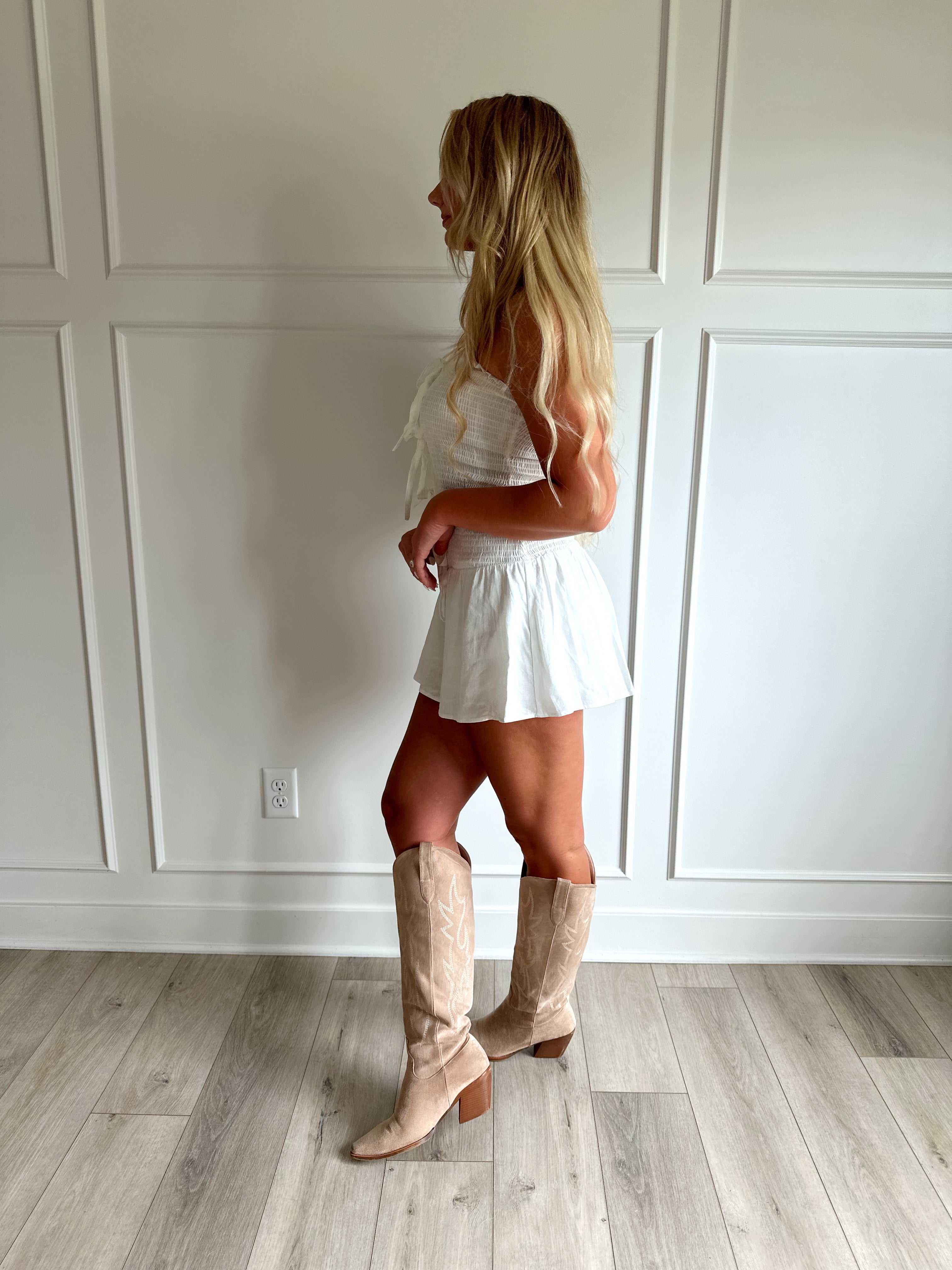 Woman wearing white smocked strapless mini dress with bow detail and clasp closure.