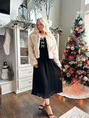Woman wearing beige faux fur coat with front pockets and clasp closure. 