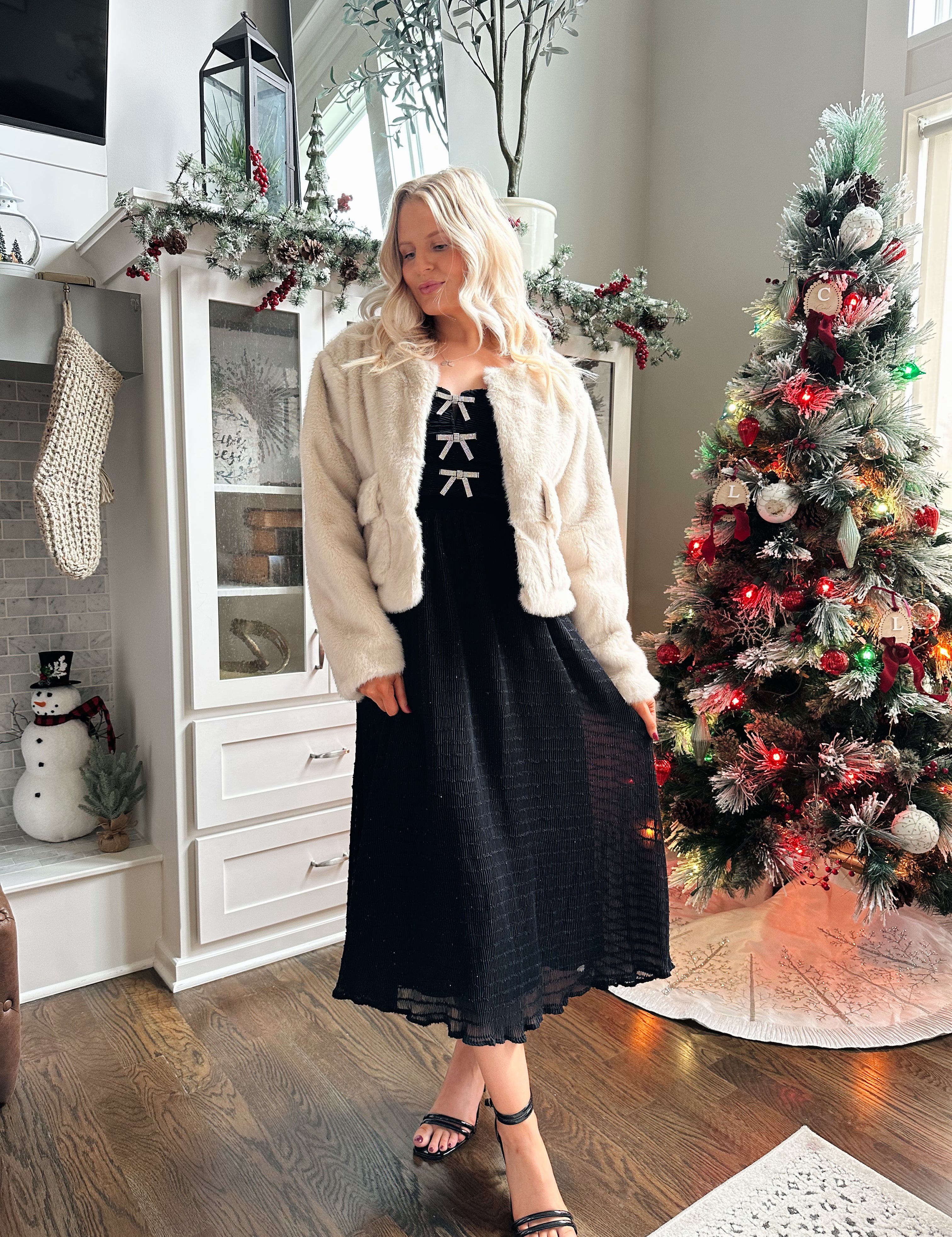 Woman wearing beige faux fur coat with front pockets and clasp closure. 