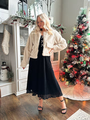 Woman wearing beige faux fur coat with front pockets and clasp closure. 