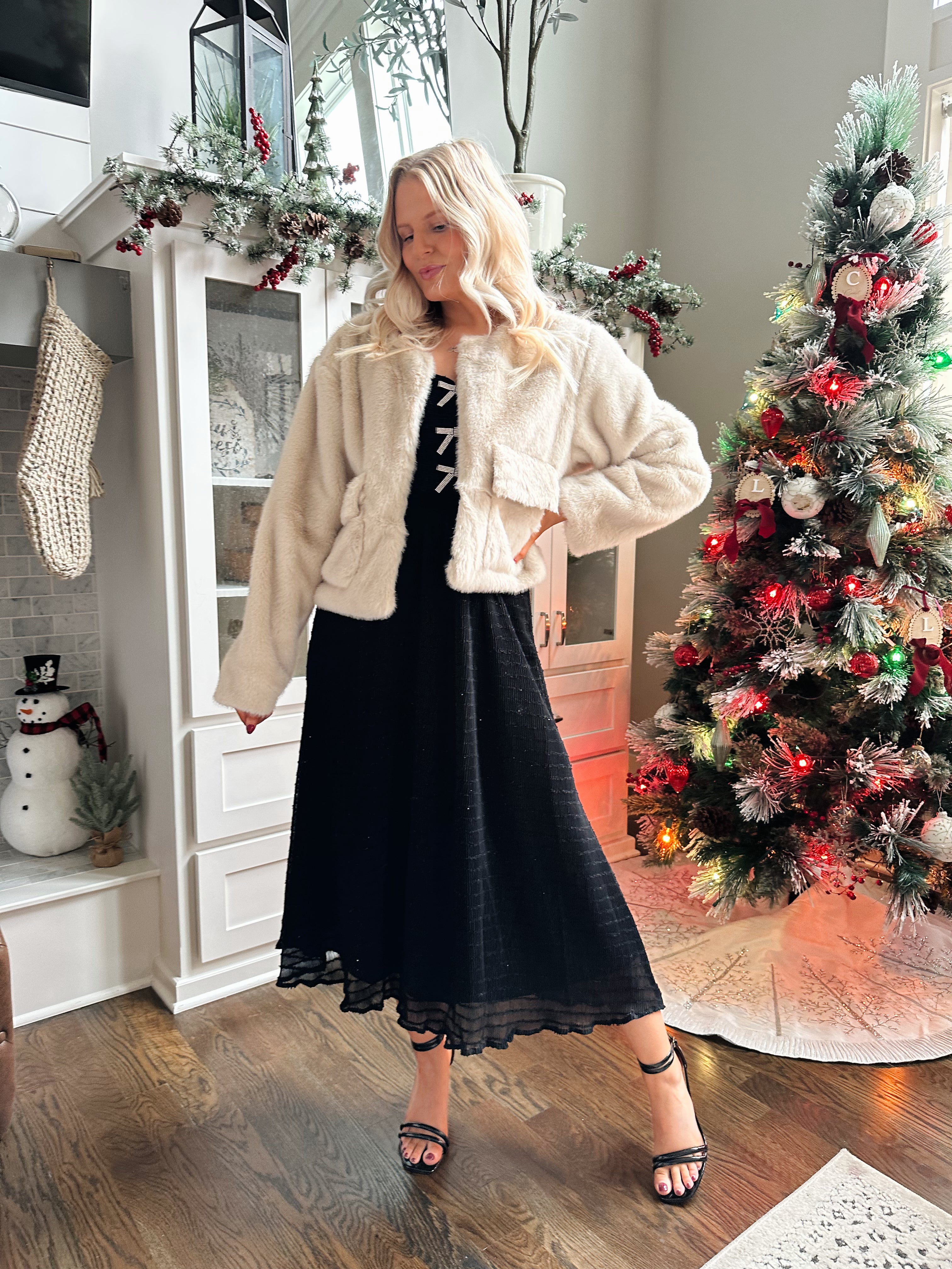 Woman wearing beige faux fur coat with front pockets and clasp closure. 