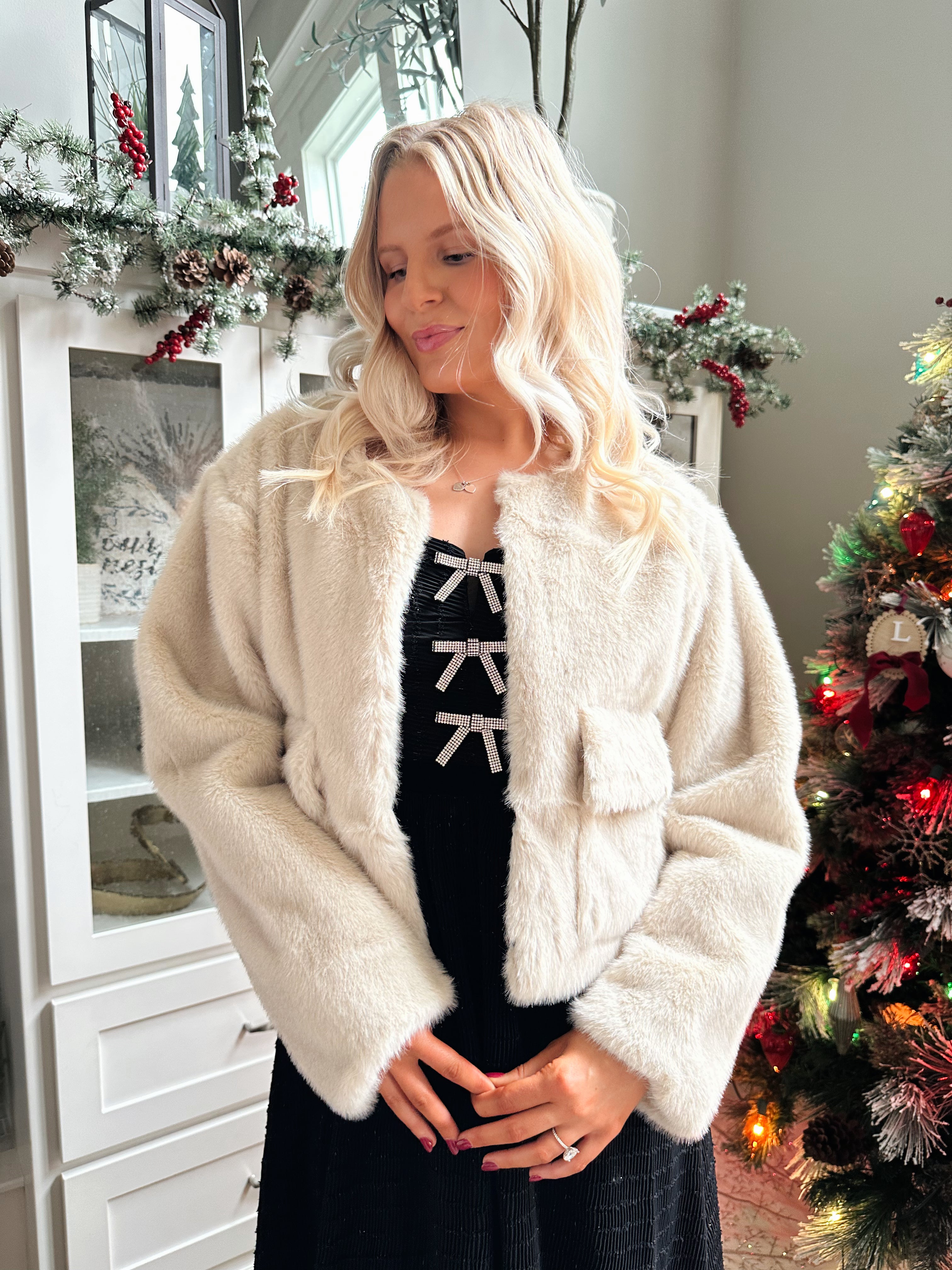 Woman wearing beige faux fur coat with front pockets and clasp closure. 