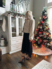Woman wearing beige faux fur coat with front pockets and clasp closure. 