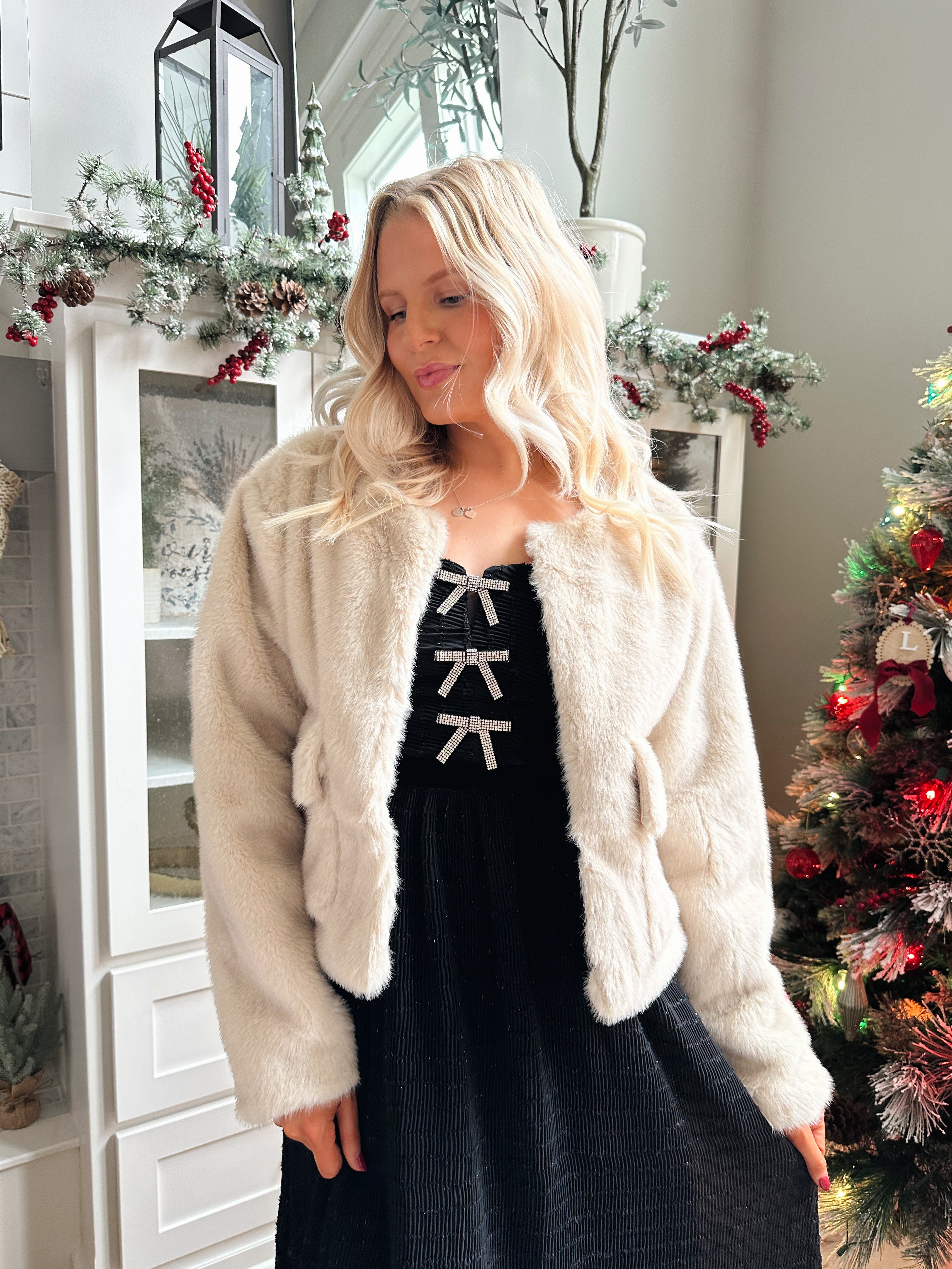 Woman wearing beige faux fur coat with front pockets and clasp closure. 