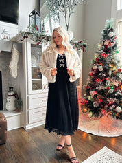 Woman wearing beige faux fur coat with front pockets and clasp closure. 